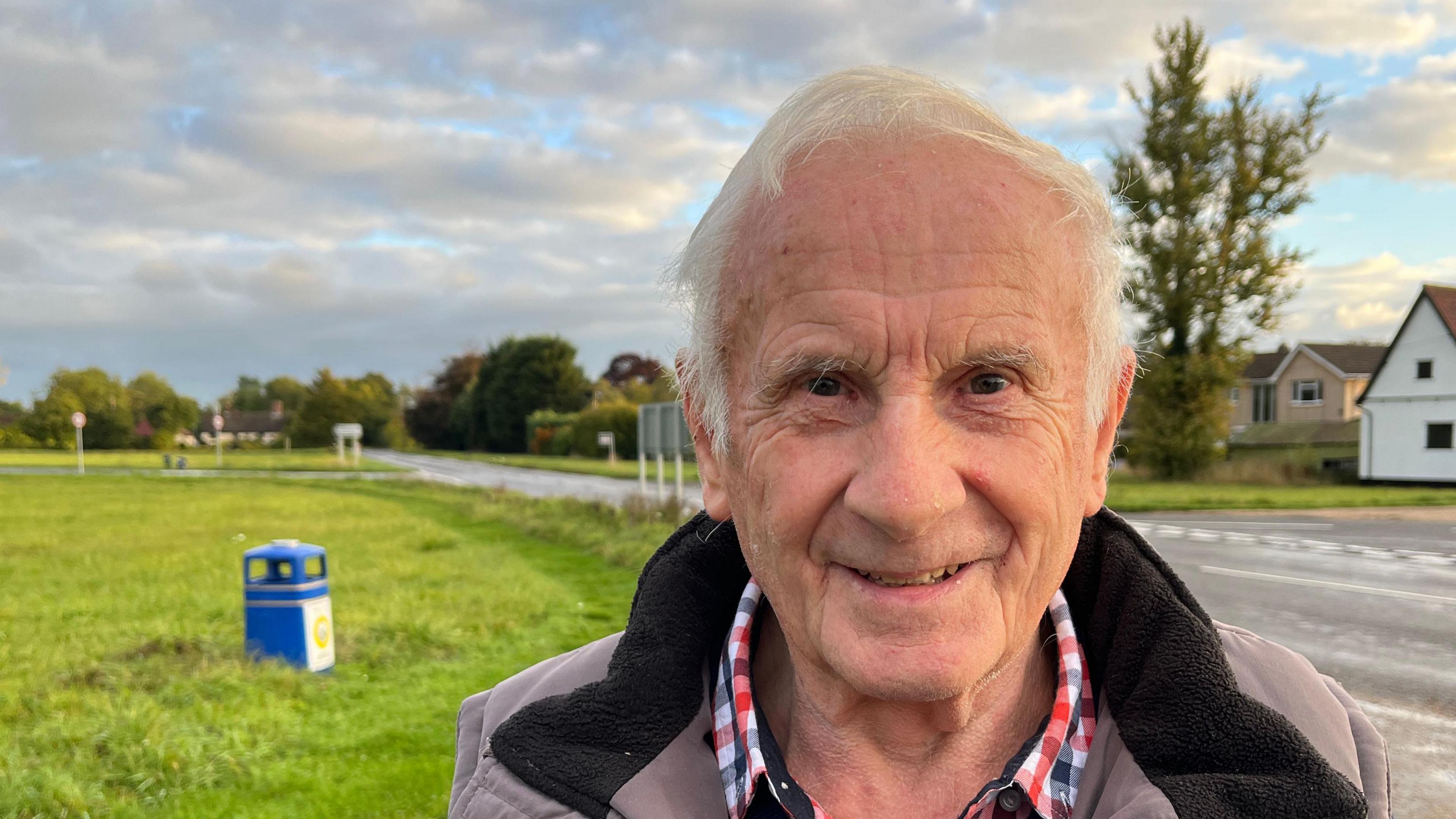 A head and shoulders image of George Cullingford. He is smiling into the camera. A green and a road can be seen in the background. 