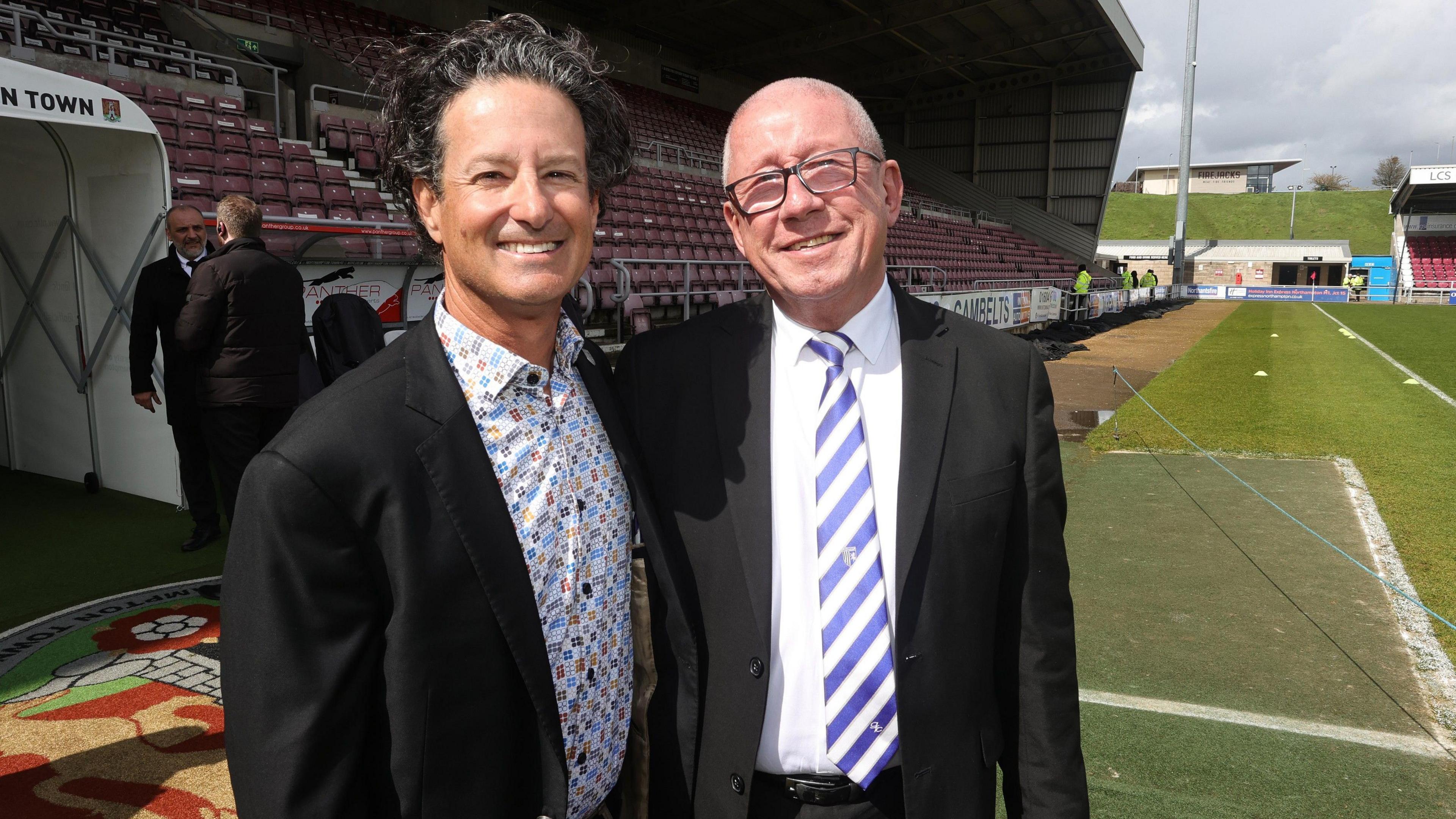 Brad Galinson and Paul Scally wearing suits and standing beside each other at Northampton Town Football Club.