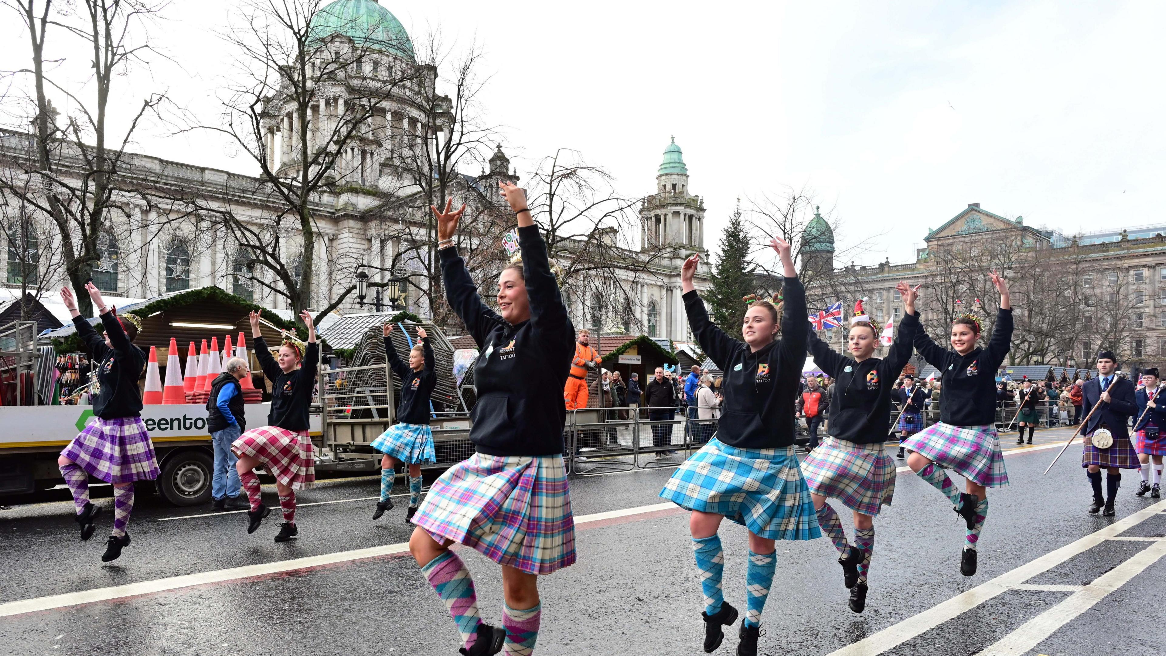 The picture shows a number of girls in kilts Highland dancing past Belfast City Hall
