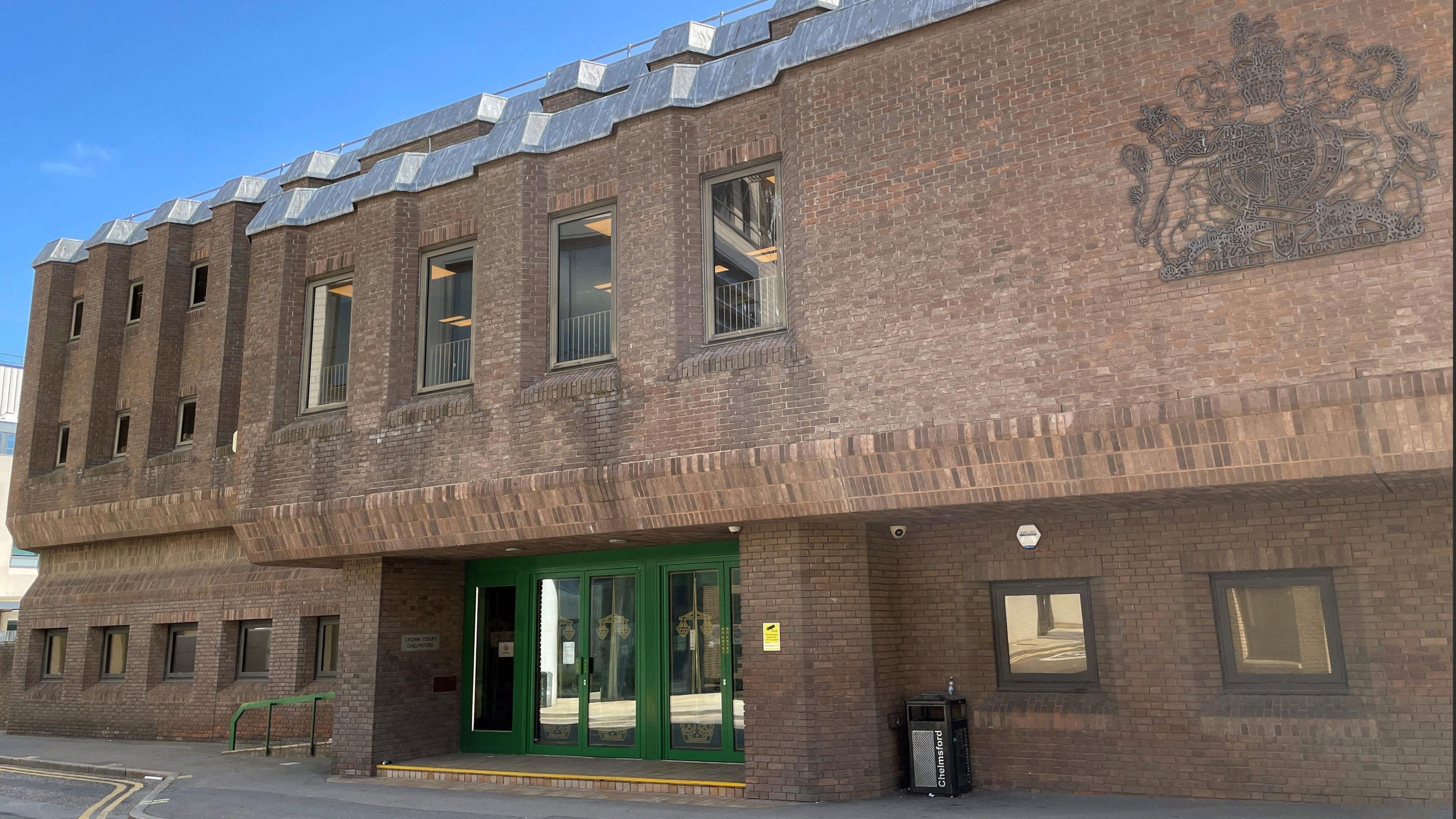 A two-storey court building dating from the 1970s or 80s. It is built of brown brick and has a large royal crest on the front. It has green doors and mirrored windows.