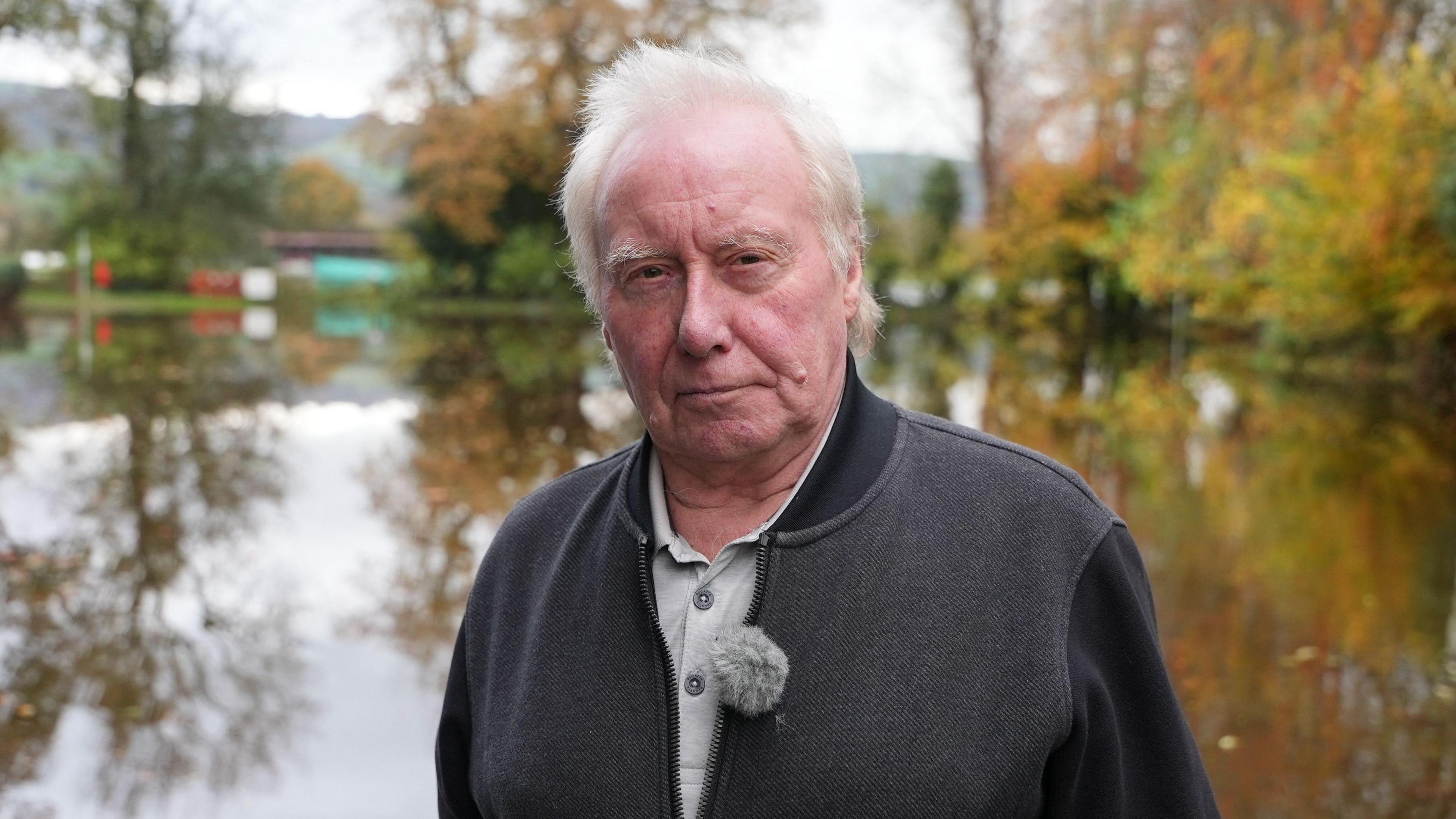 Cynghorydd dros ardal Uwch Conwy, Dilwyn Roberts yn sefyll o flaen llyn. Mae ganddo wallt gwyn ac mae'n gwisgo siaced lwyd.