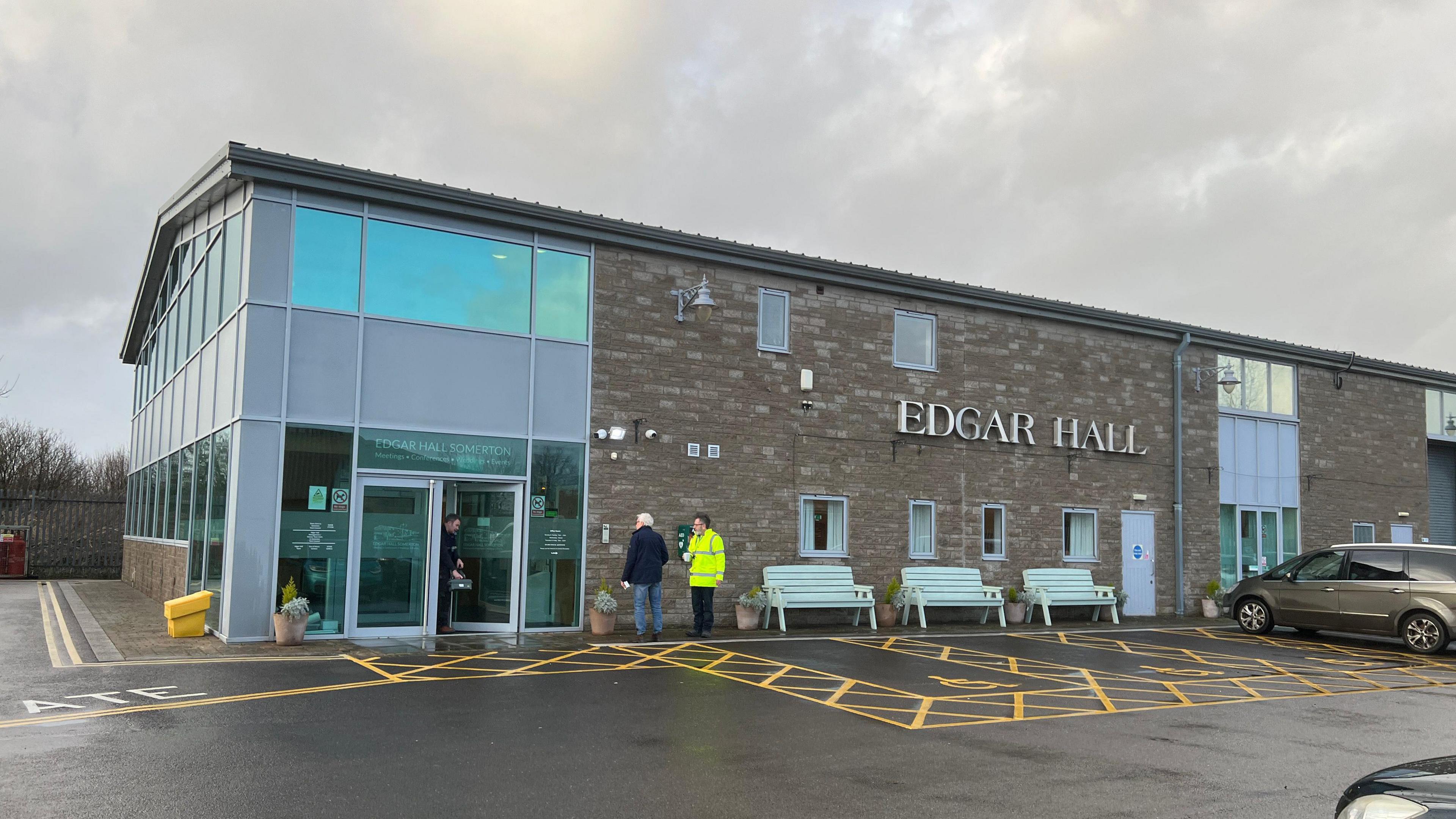 A hall and car park with people standing outside