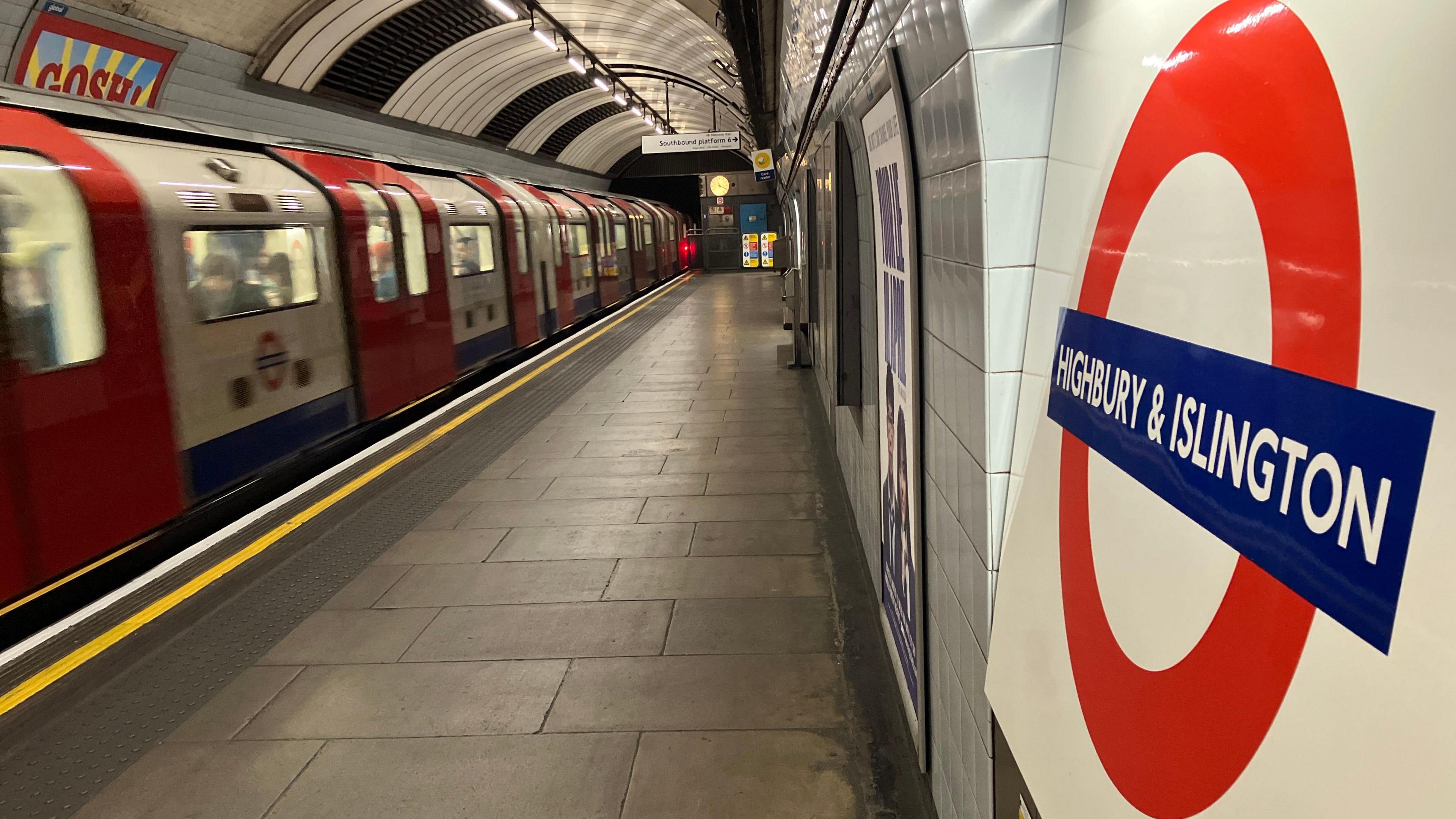 Tube train (left) arrives on empty platform at Highbury and Islington station with station roundel on the right