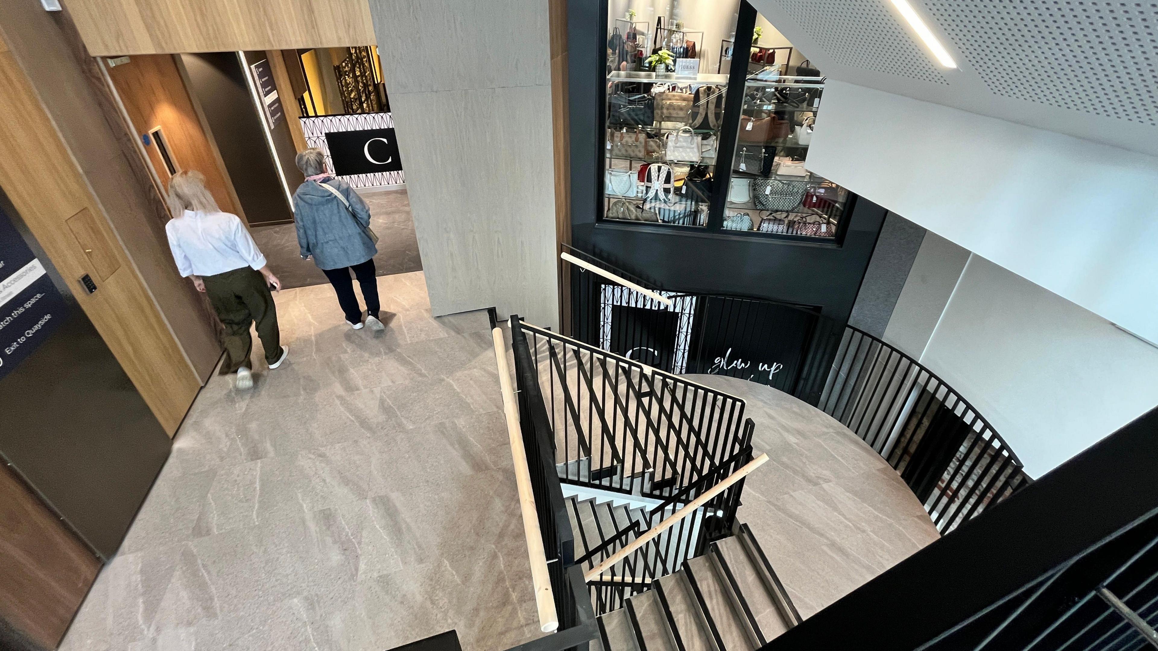 A modern stairwell with two people walking towards the shop floor.