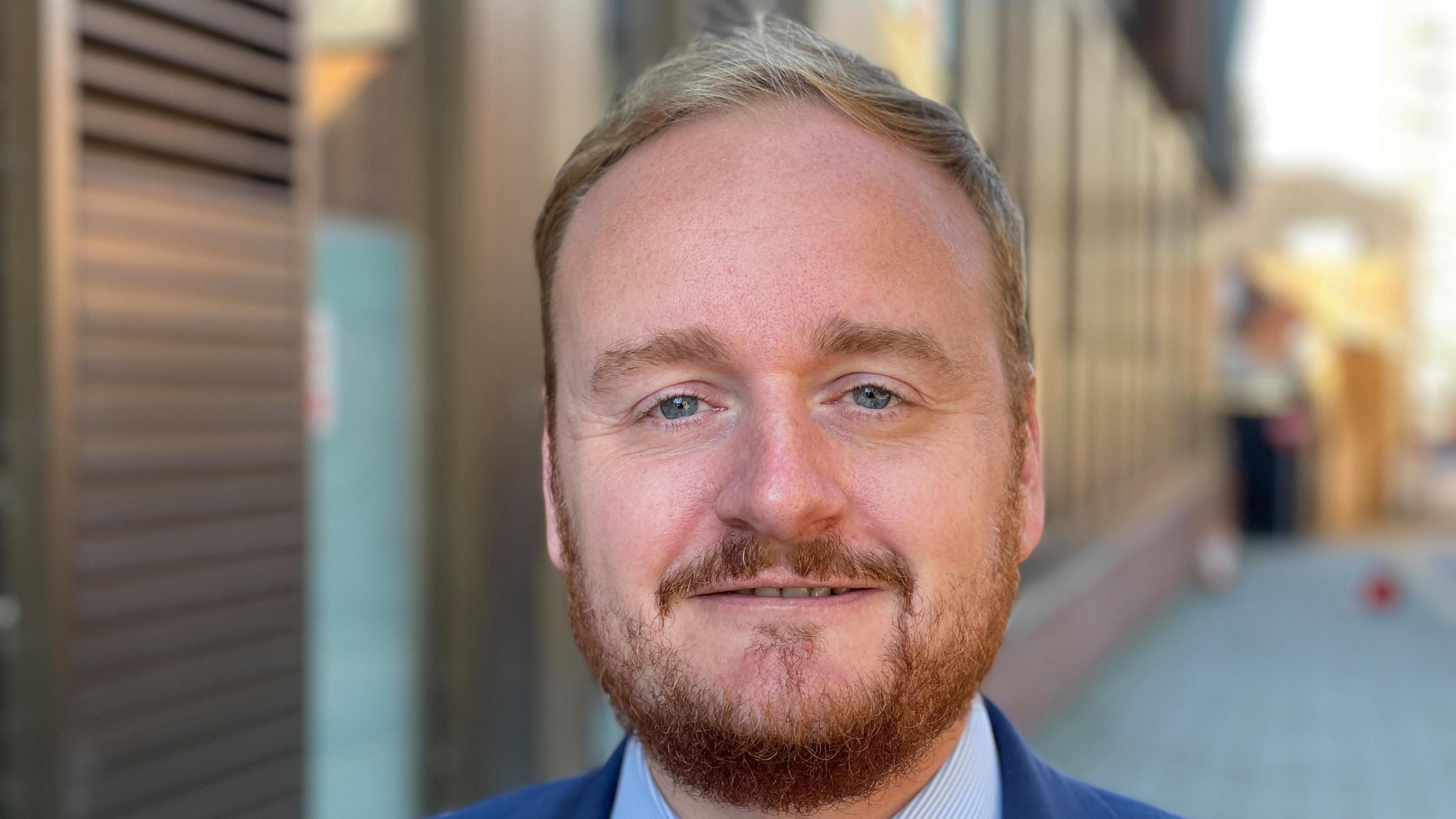 A smiling man with short ginger hair and a ginger beard