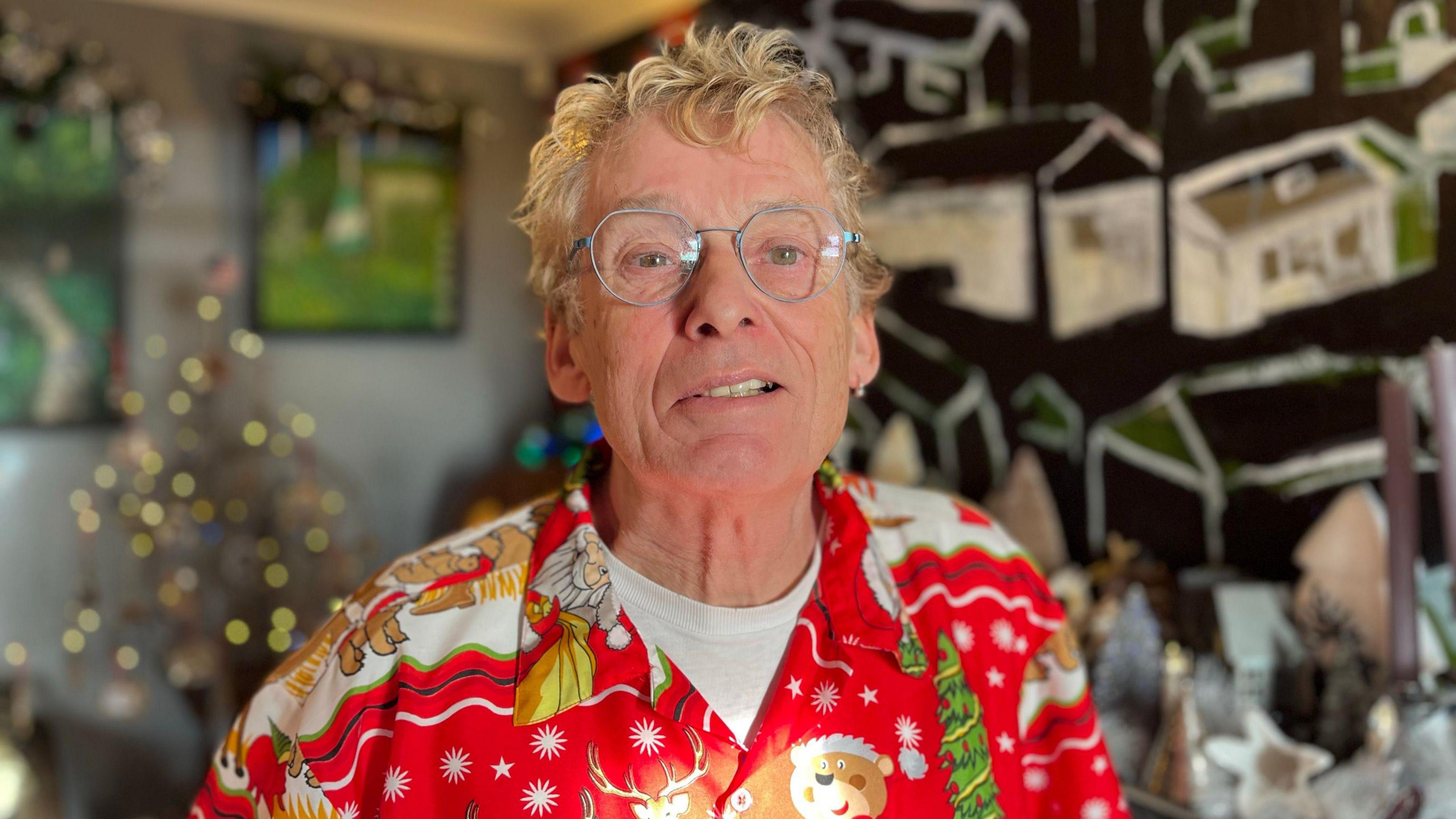 Geoff Stonebanks wearing a red christmas themed shirt with a christmas tree behind him