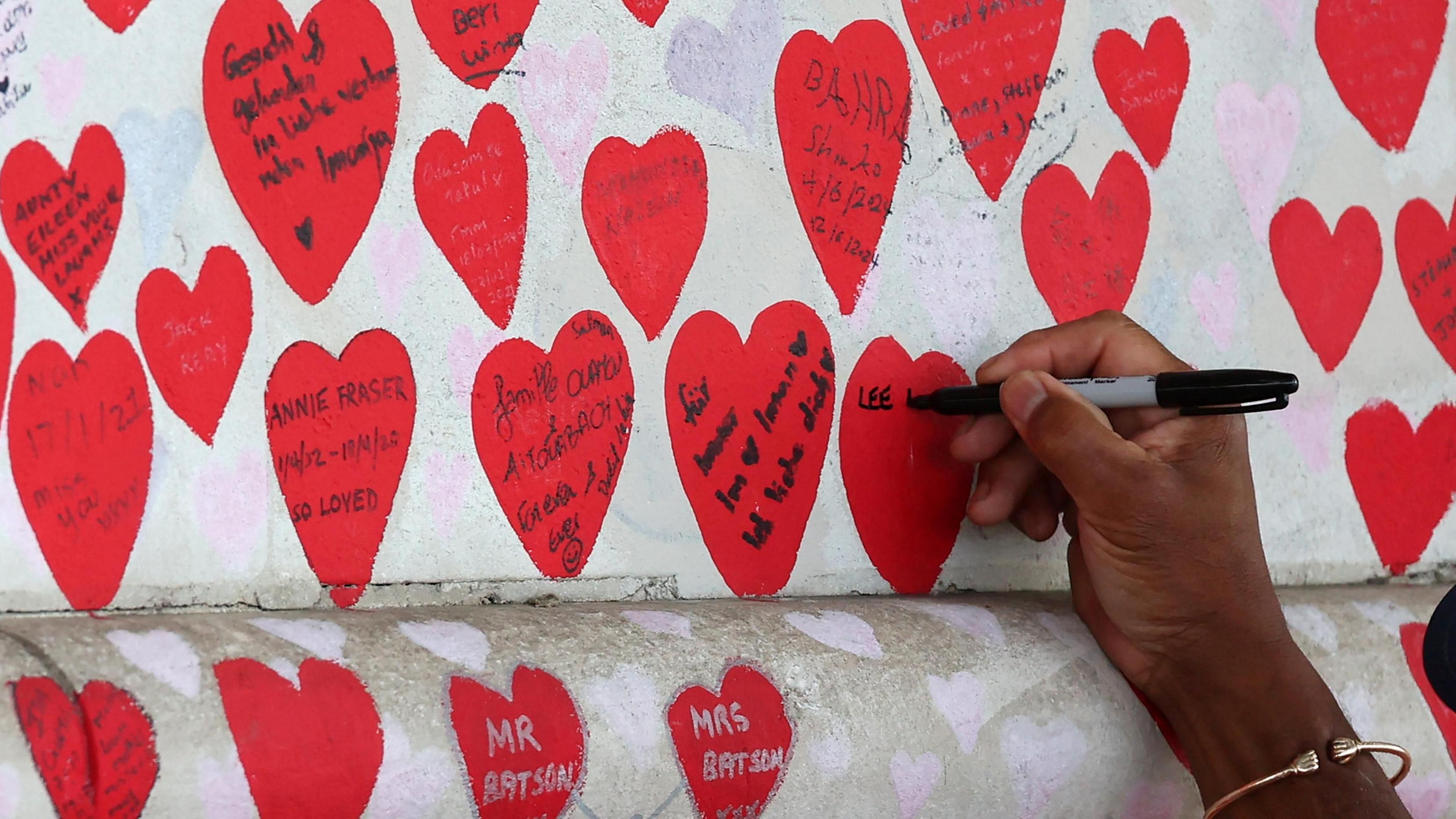 Someone writes a commemoration inside a red heart painted on the national covid memorial wall.