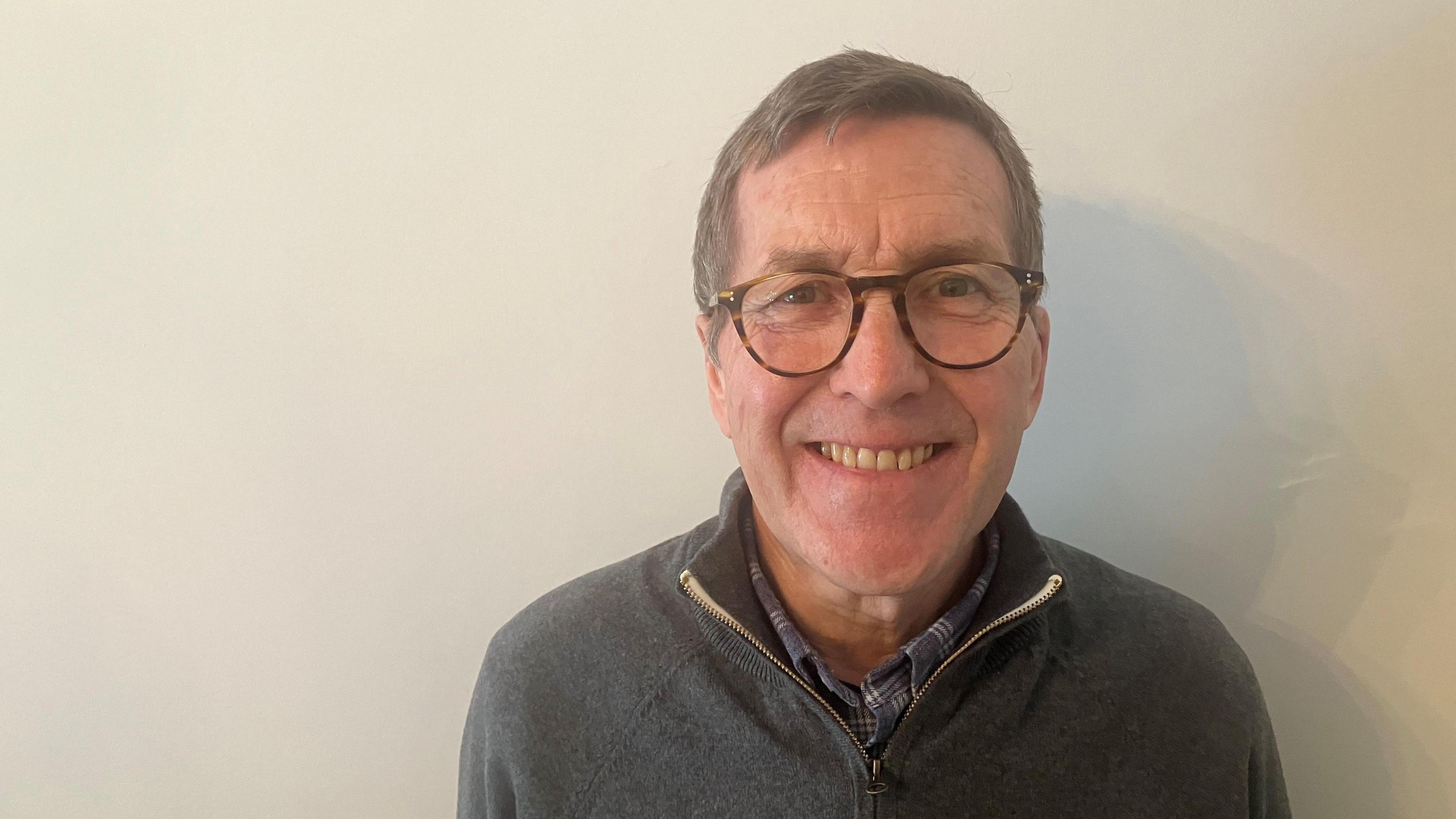 Photograph of Mark Hunter, the Liberal Democrat leader of Stockport Council. He's standing in front of a white wall.