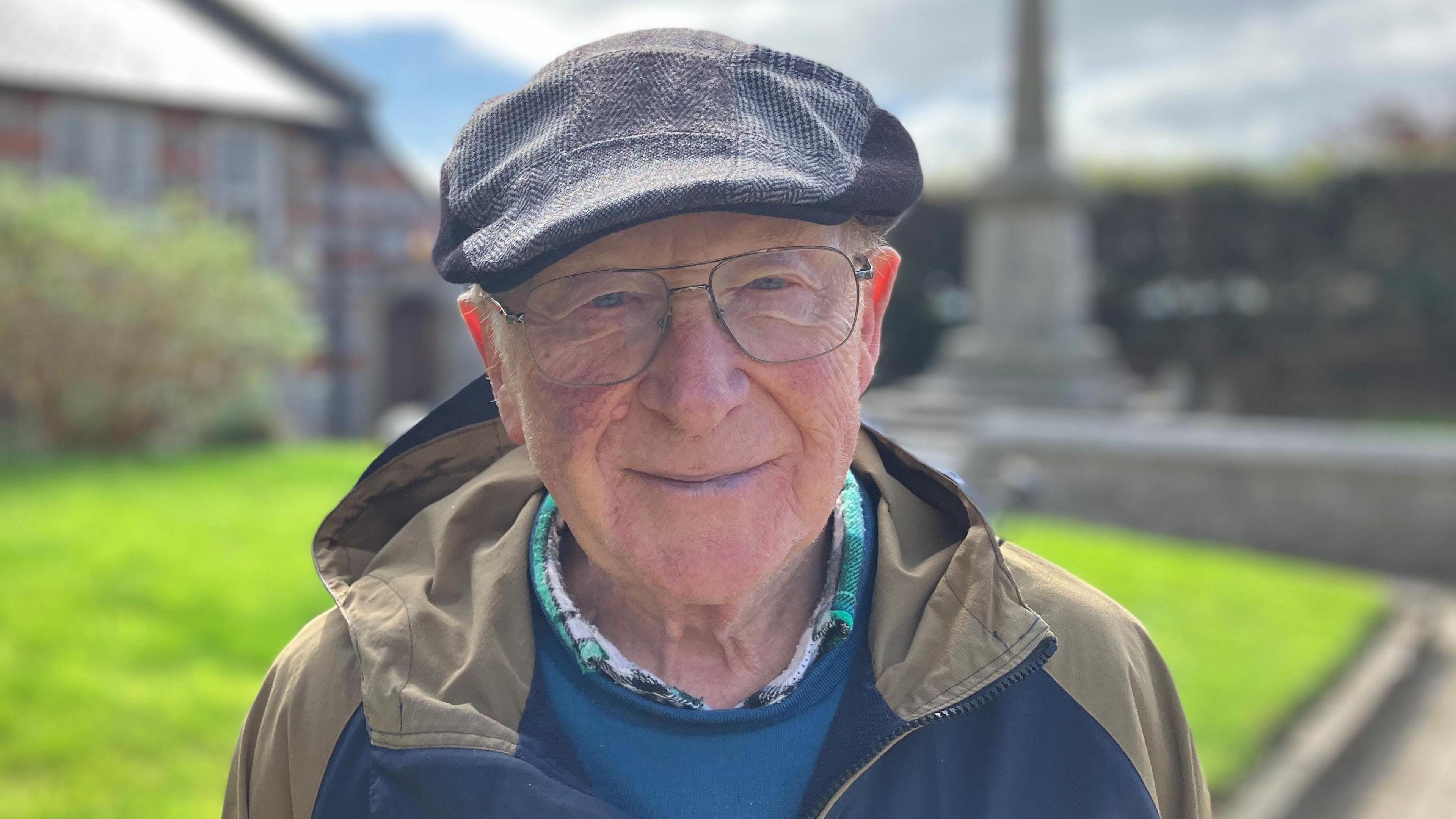 Man in glasses with flat cap in front of World War One memorial 