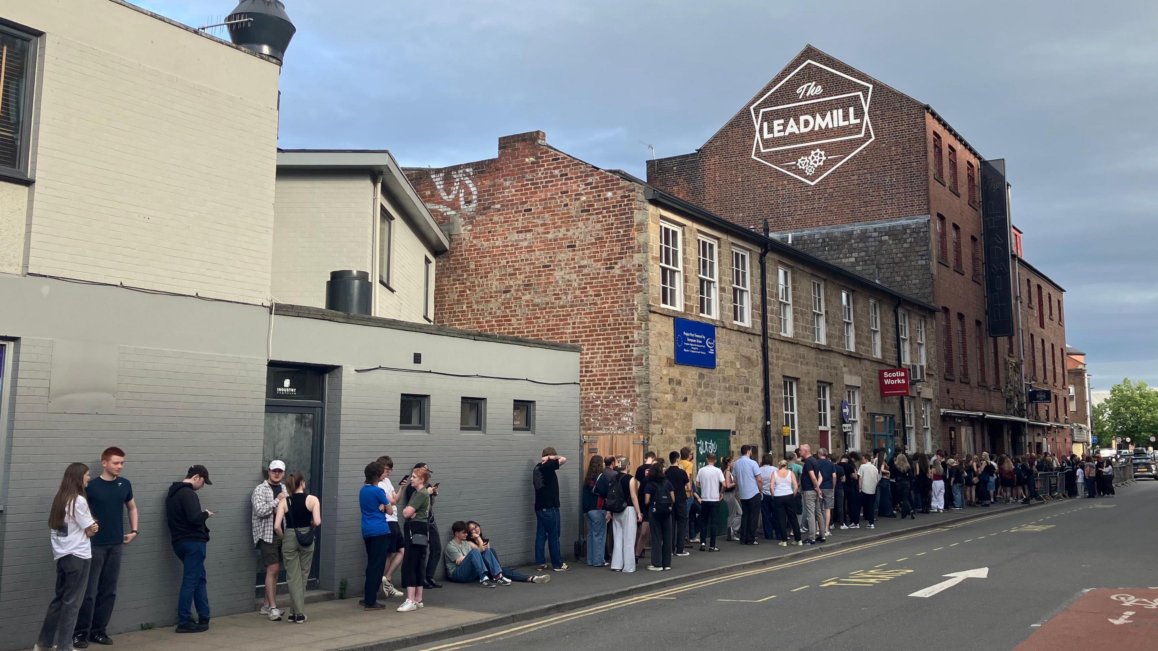 Long queue of people outside The Leadmill building, with "The Leadmill" sign above them, painted on the side of a redbrick building.