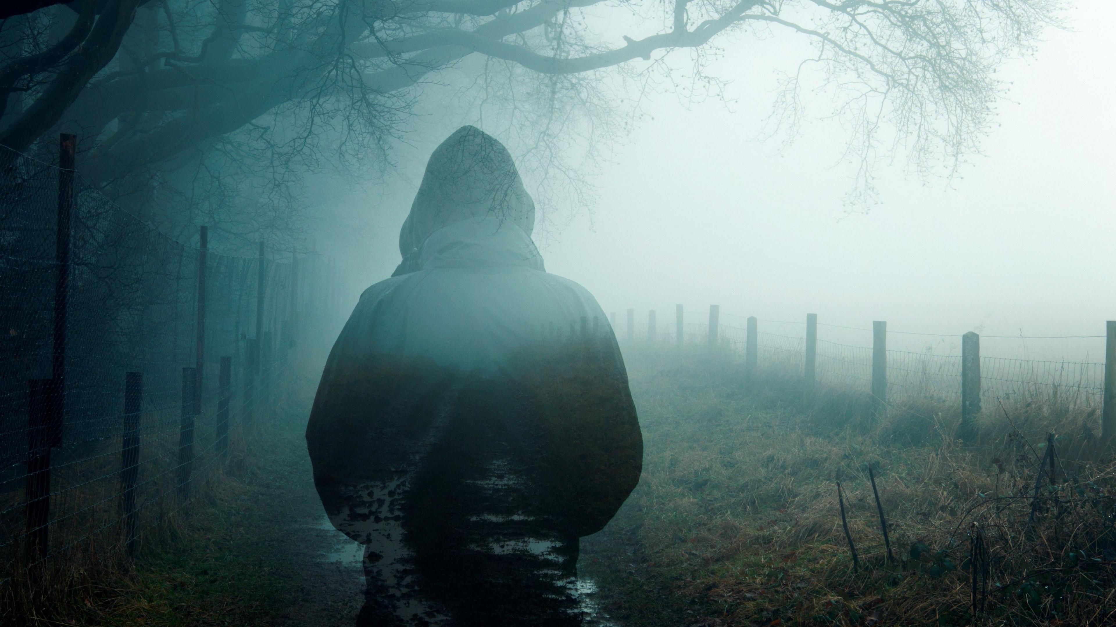 A person wearing a hoody and disappearing as they walk down a deserted country road.