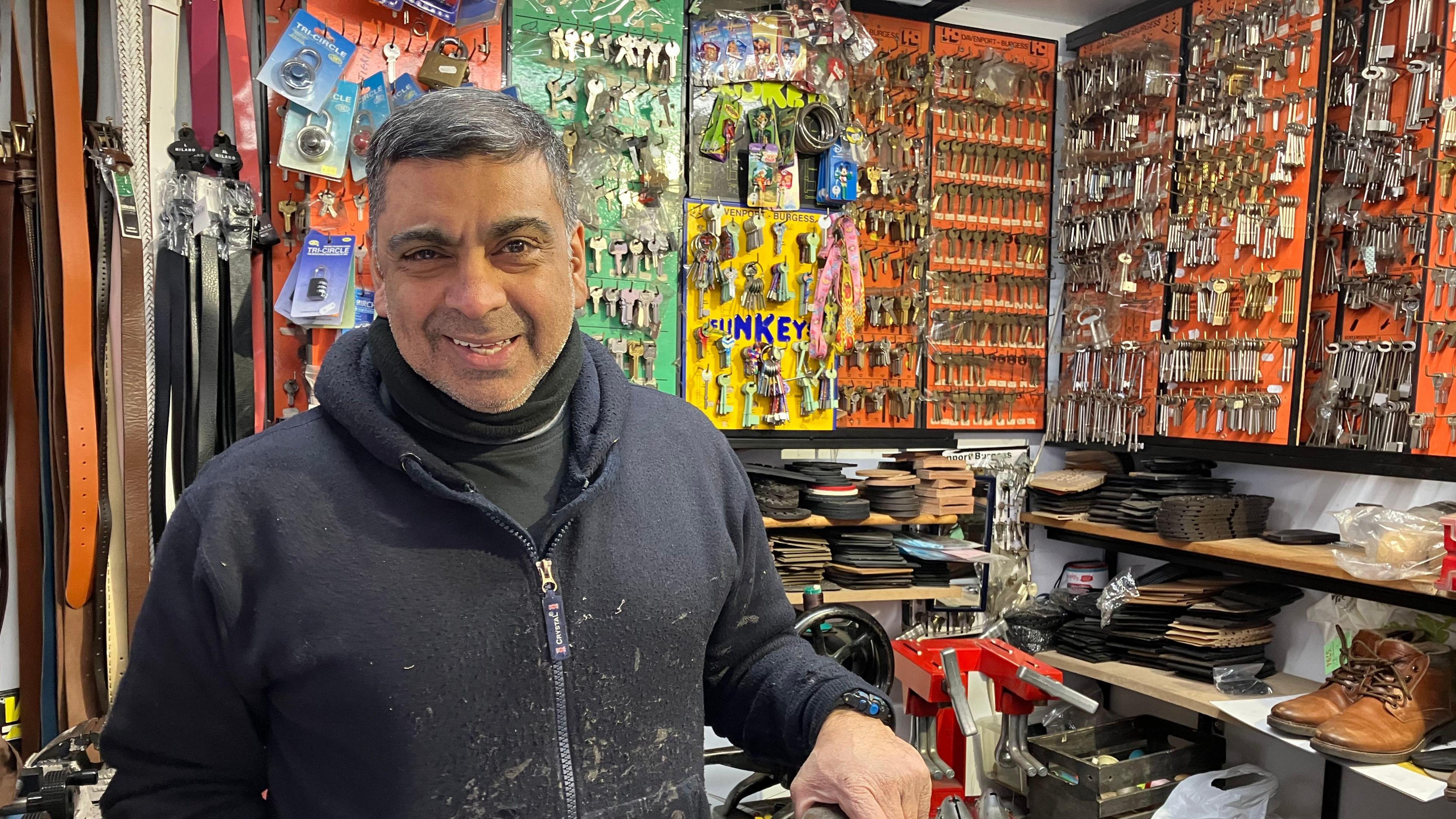 A market trader stood in front of an array of belts, shoe parts and keys