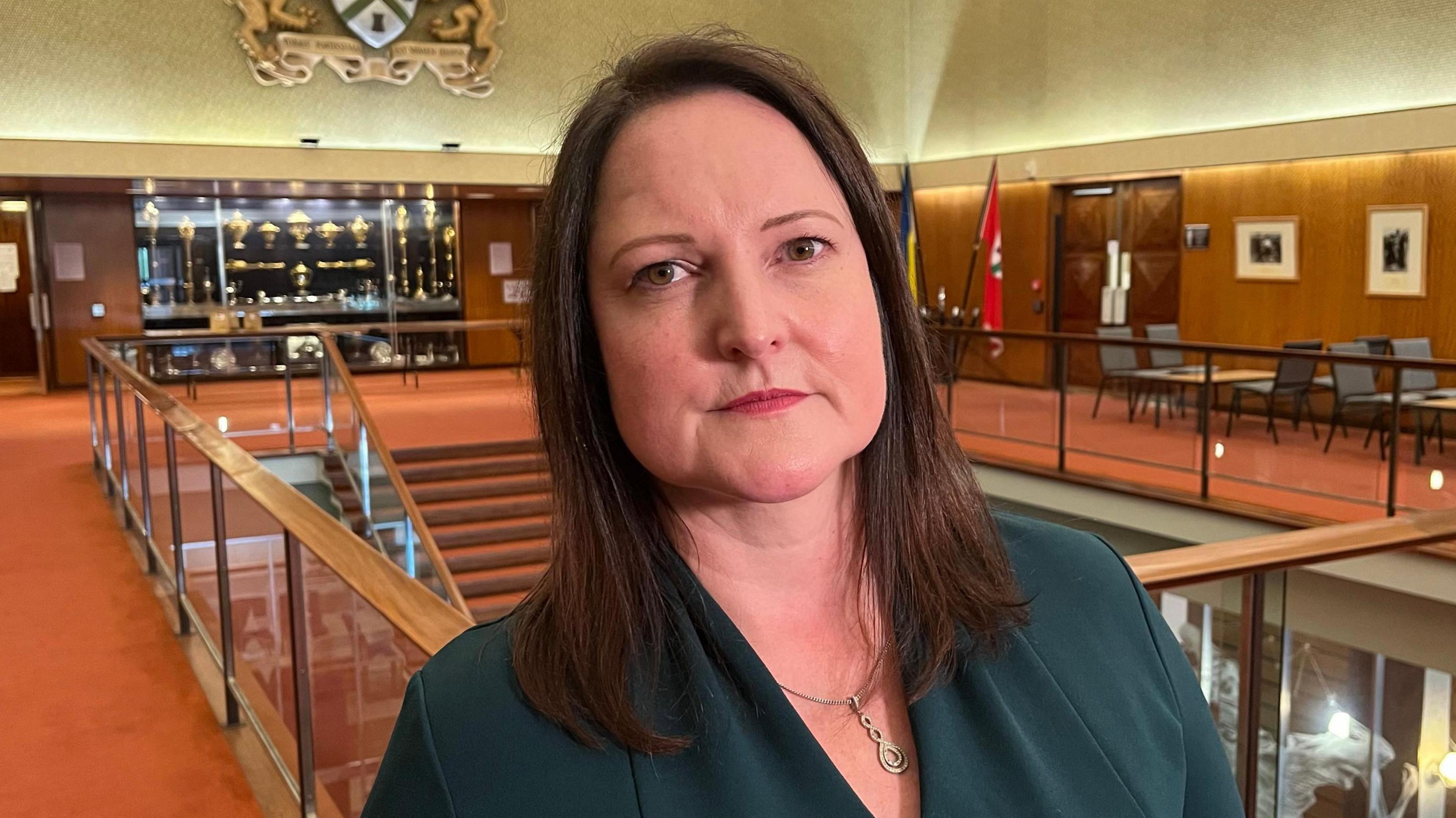 Alison Hernandez wearing a green V-necked top with a gold necklace. She has shoulder-length brown hair.