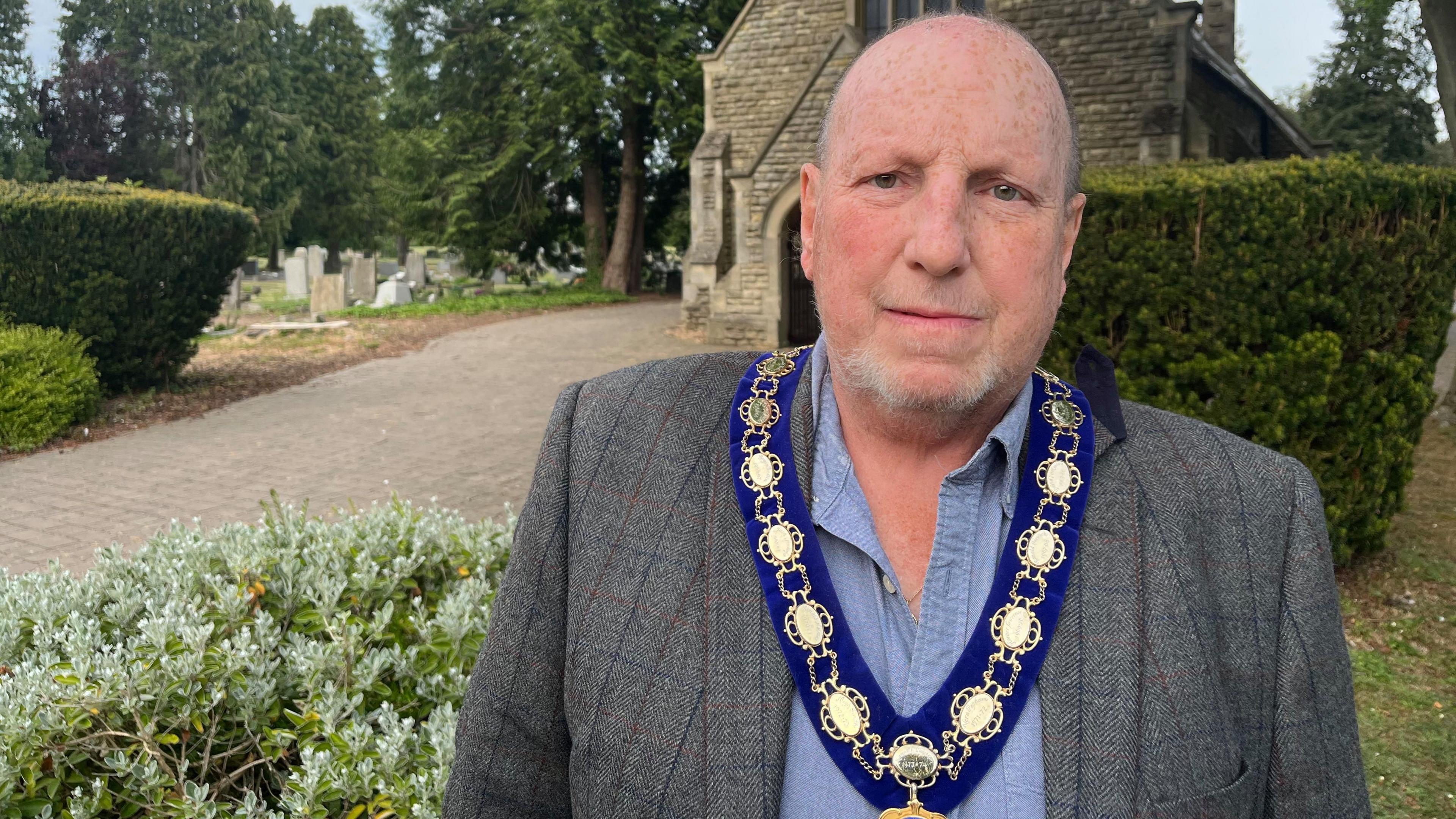 Bald man with mayoral chains around his next stood in front of a church.