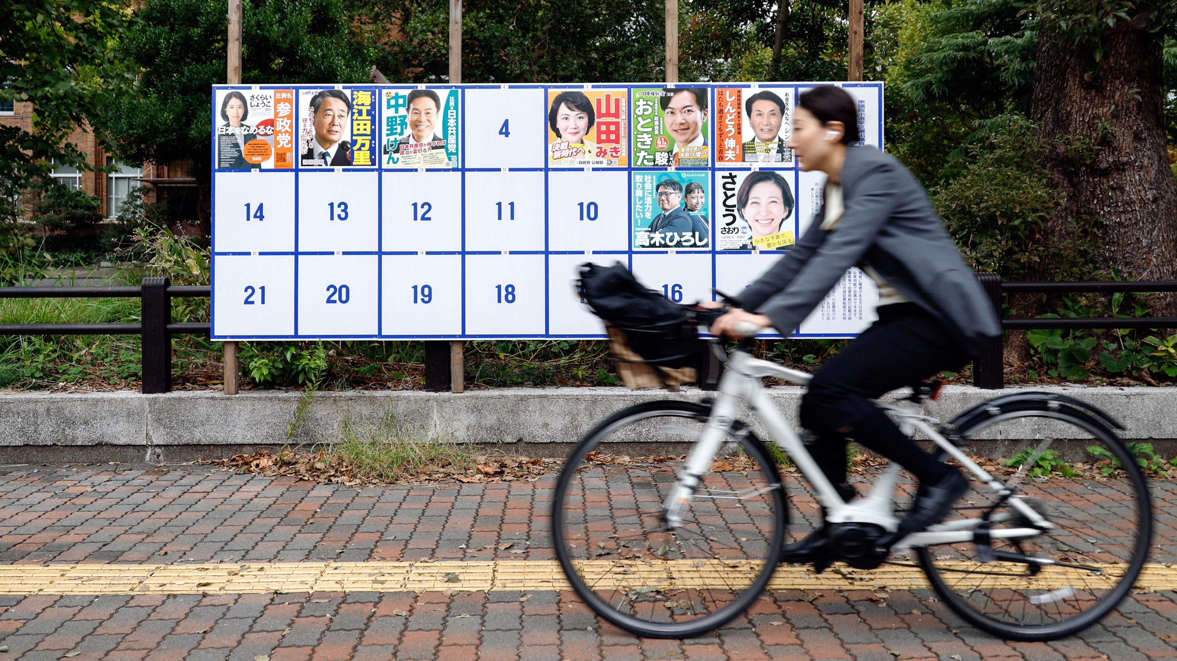 A cyclist passes a board displaying campaign posters of candidates running for the upcoming general elections in Tokyo, Japan.