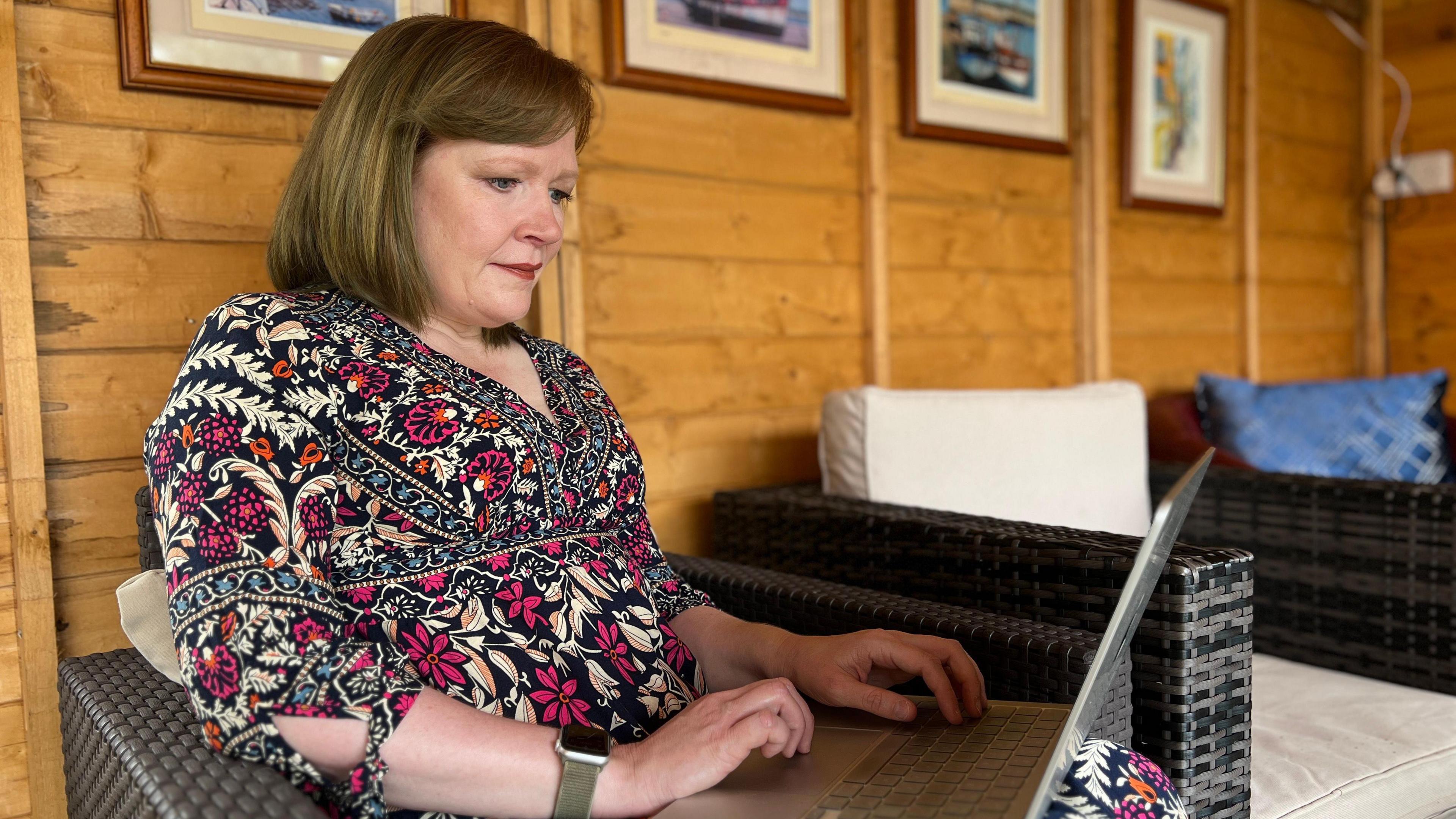 Lorna sits on a chair as she works on cancer.je website on a laptop