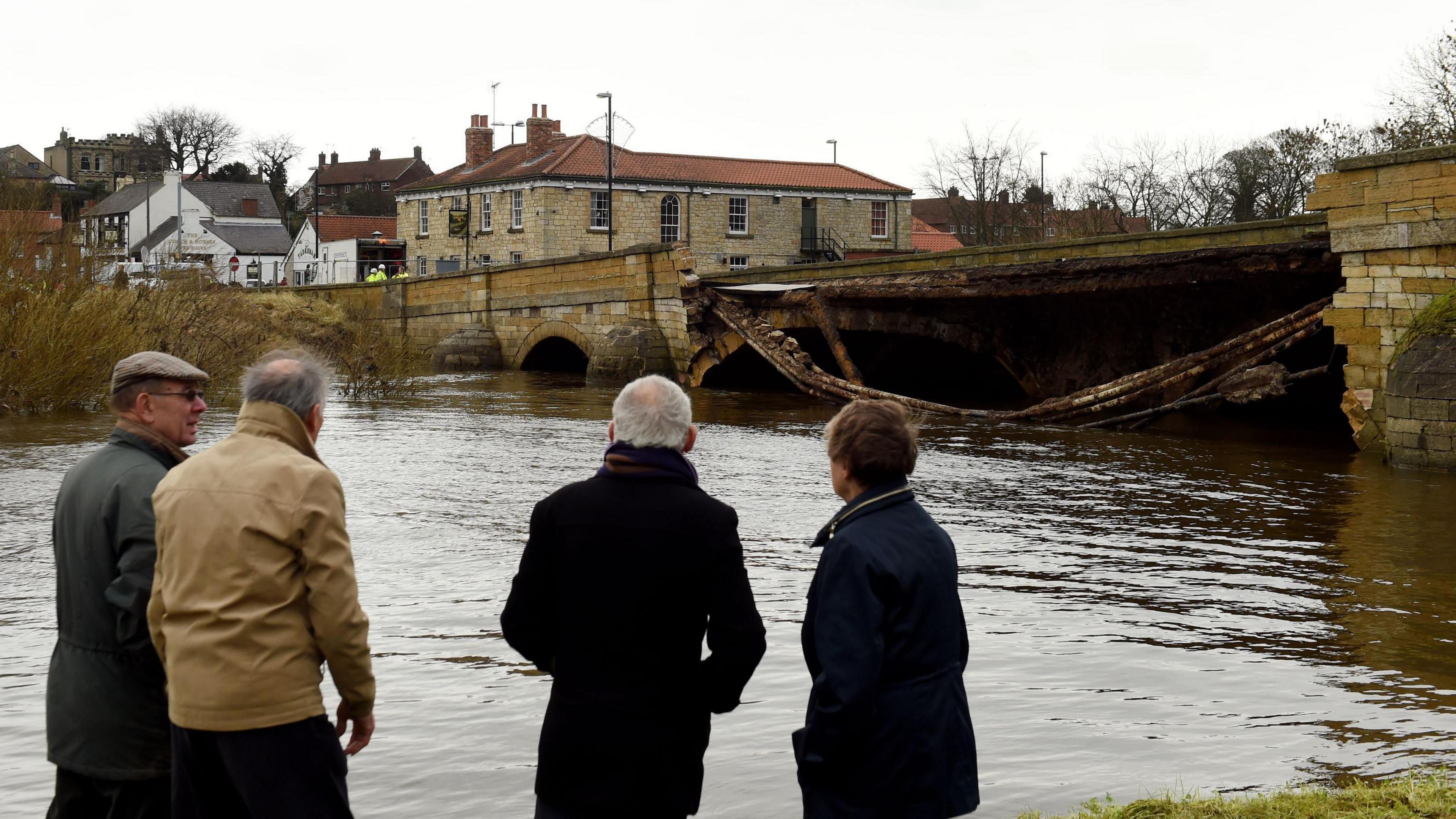 Residents view damage to Tadcaster's bridge following heavy flooding over Christmas in 2015. A section of the bridge has collapsed into the river, with contractors working at the far end of the bridge.