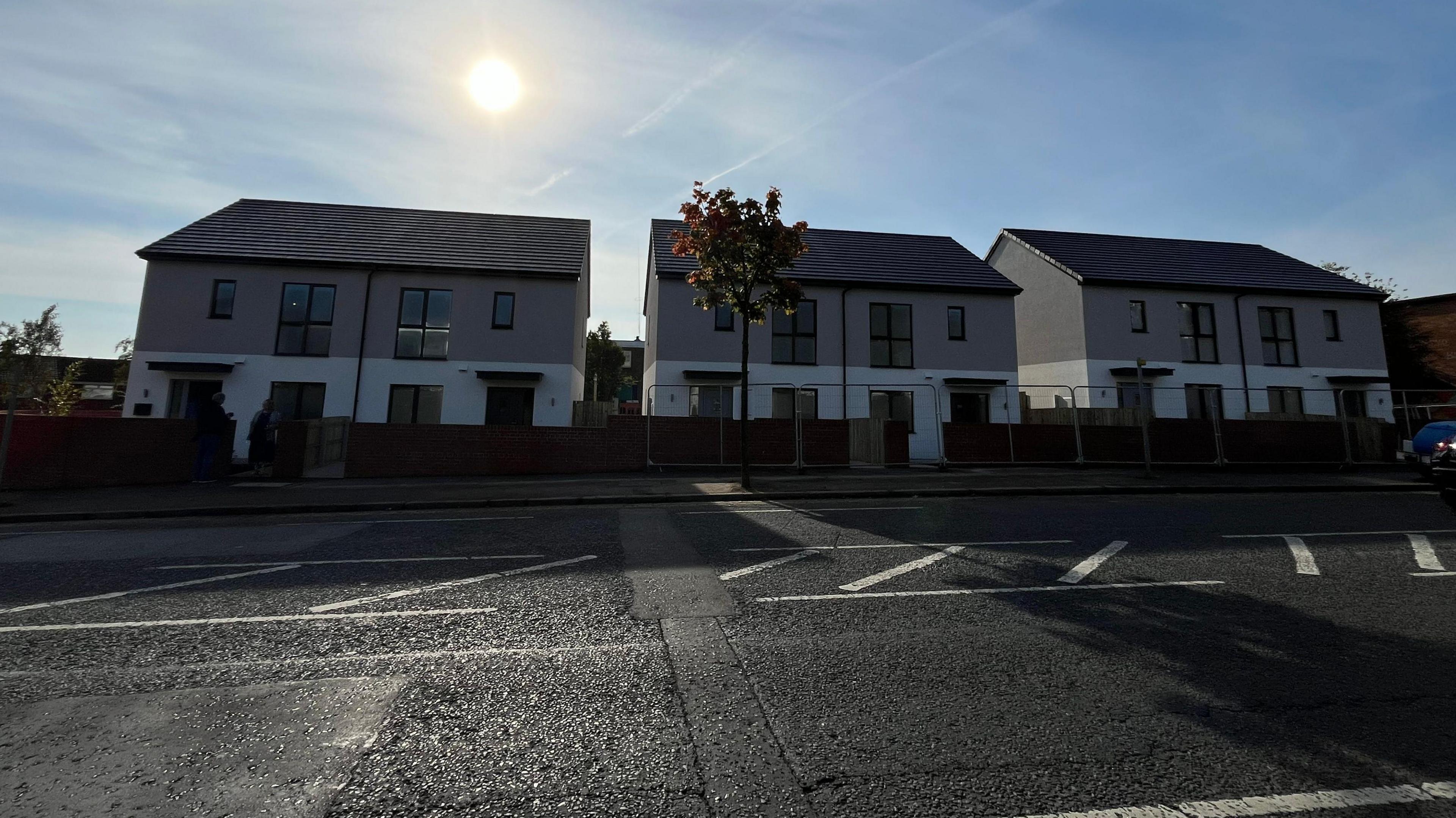 Six semi detached new build homes, with a blue sky and sun lingering above one of the houses. 