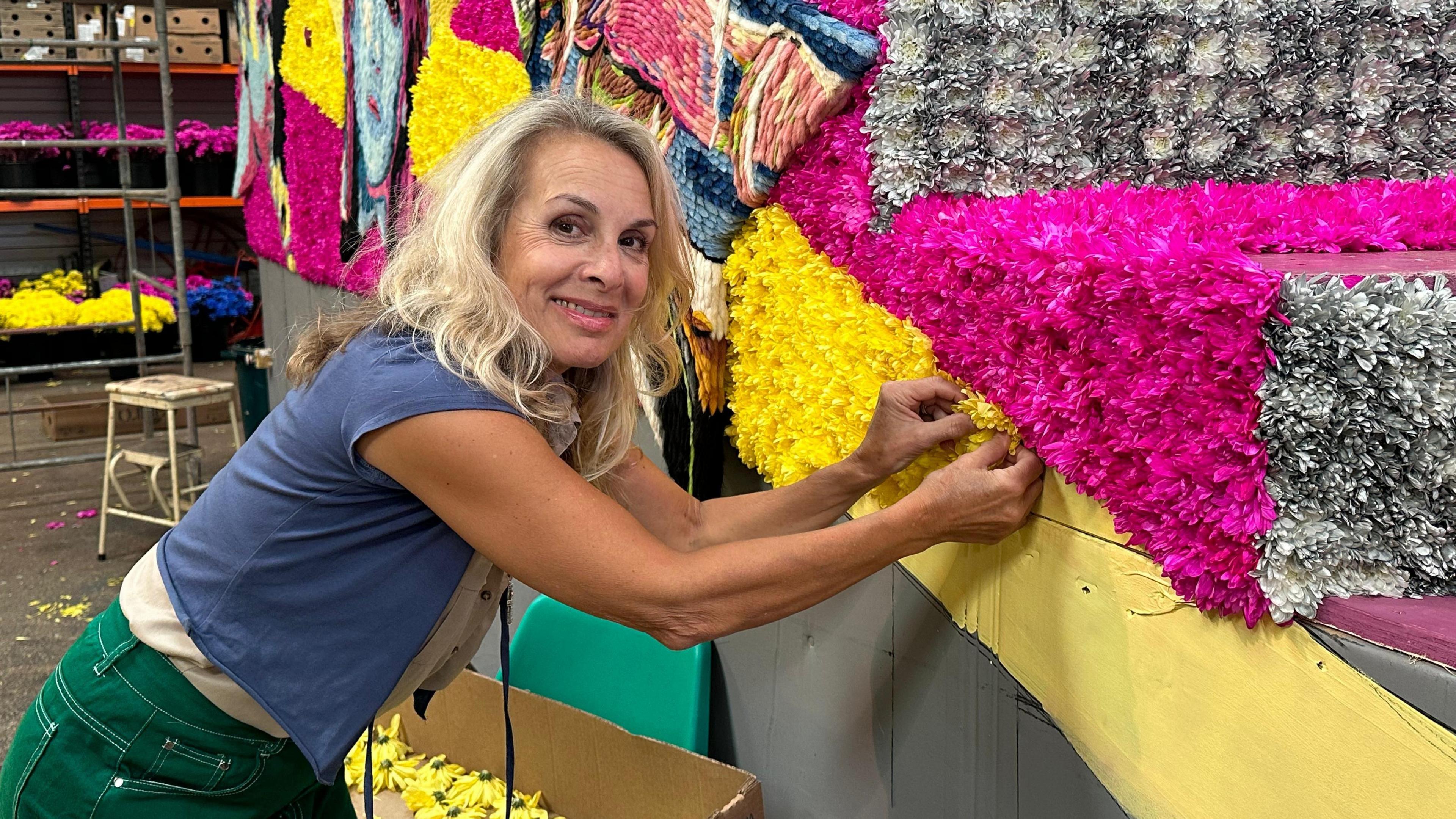 Jay Aston leaning in and sticking a yellow flower on the St Peter float which is yellow and pink stripes