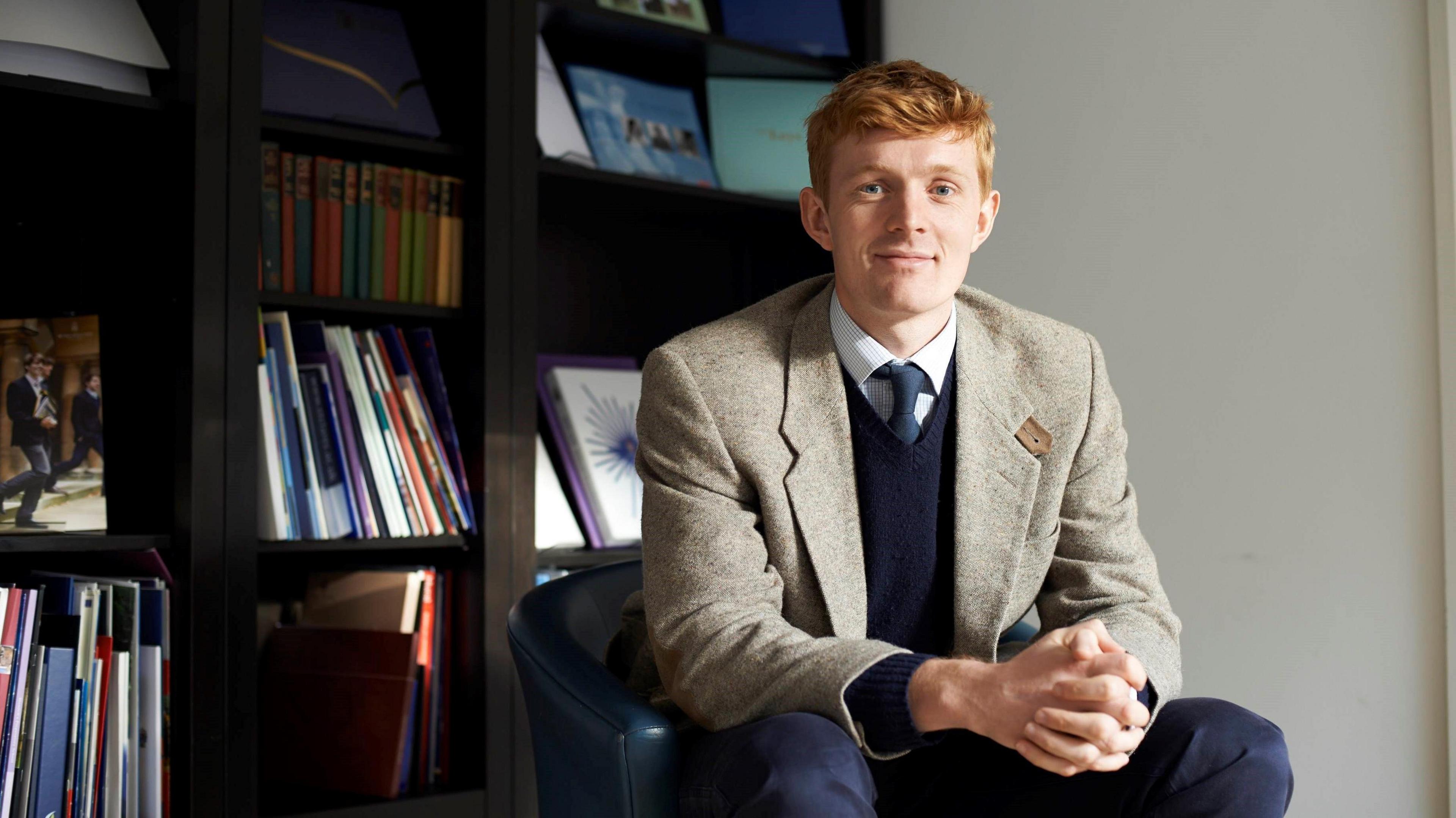 An image of Will Orr-Ewing sat in front of shelves filled with books