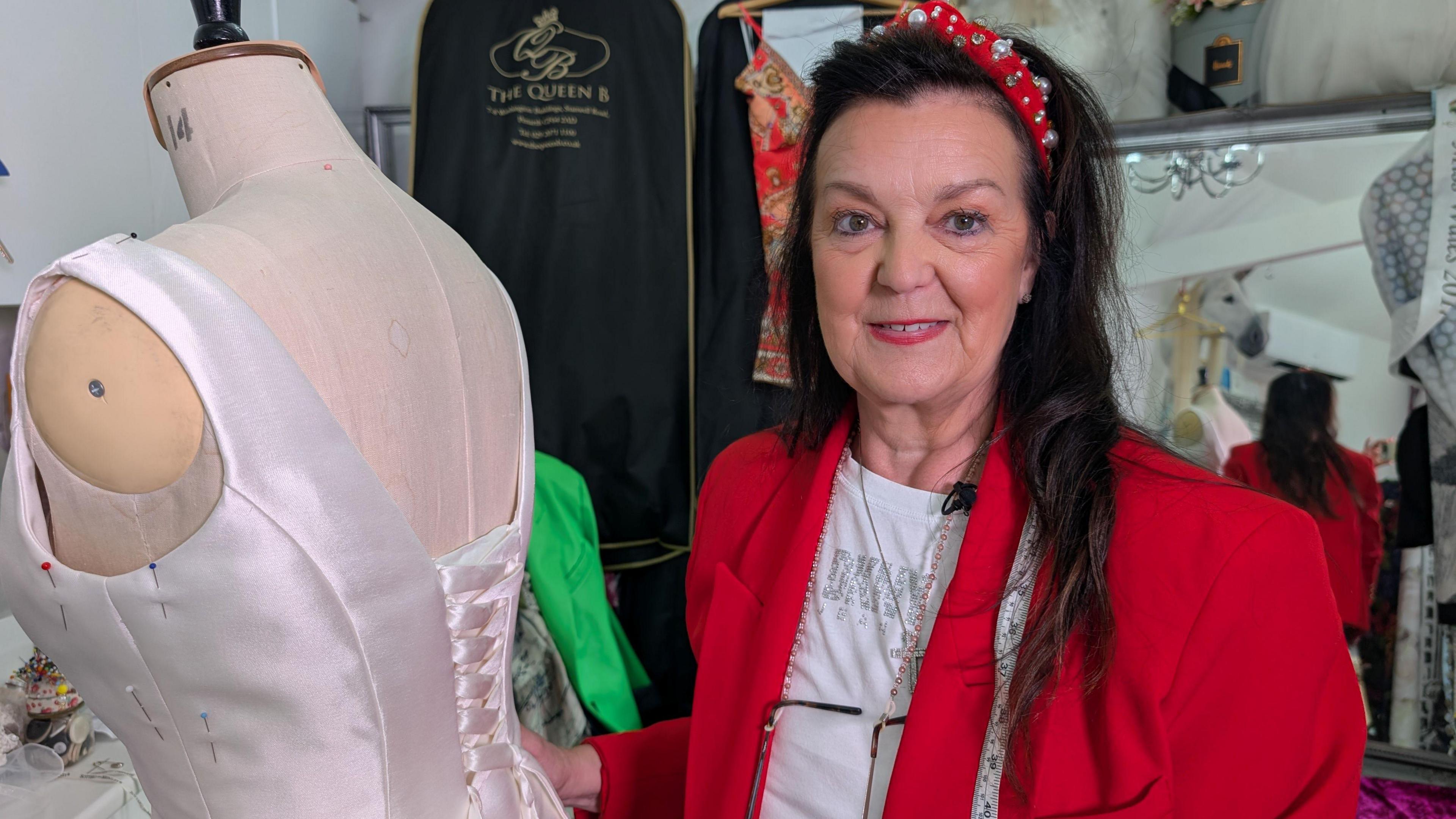 In this picture Angie is smiling at the camera as she stands next to a mannequin. Angie wears a red blazer and a white t-shirt. She's also wearing a sparkly red headband and has long black hair.