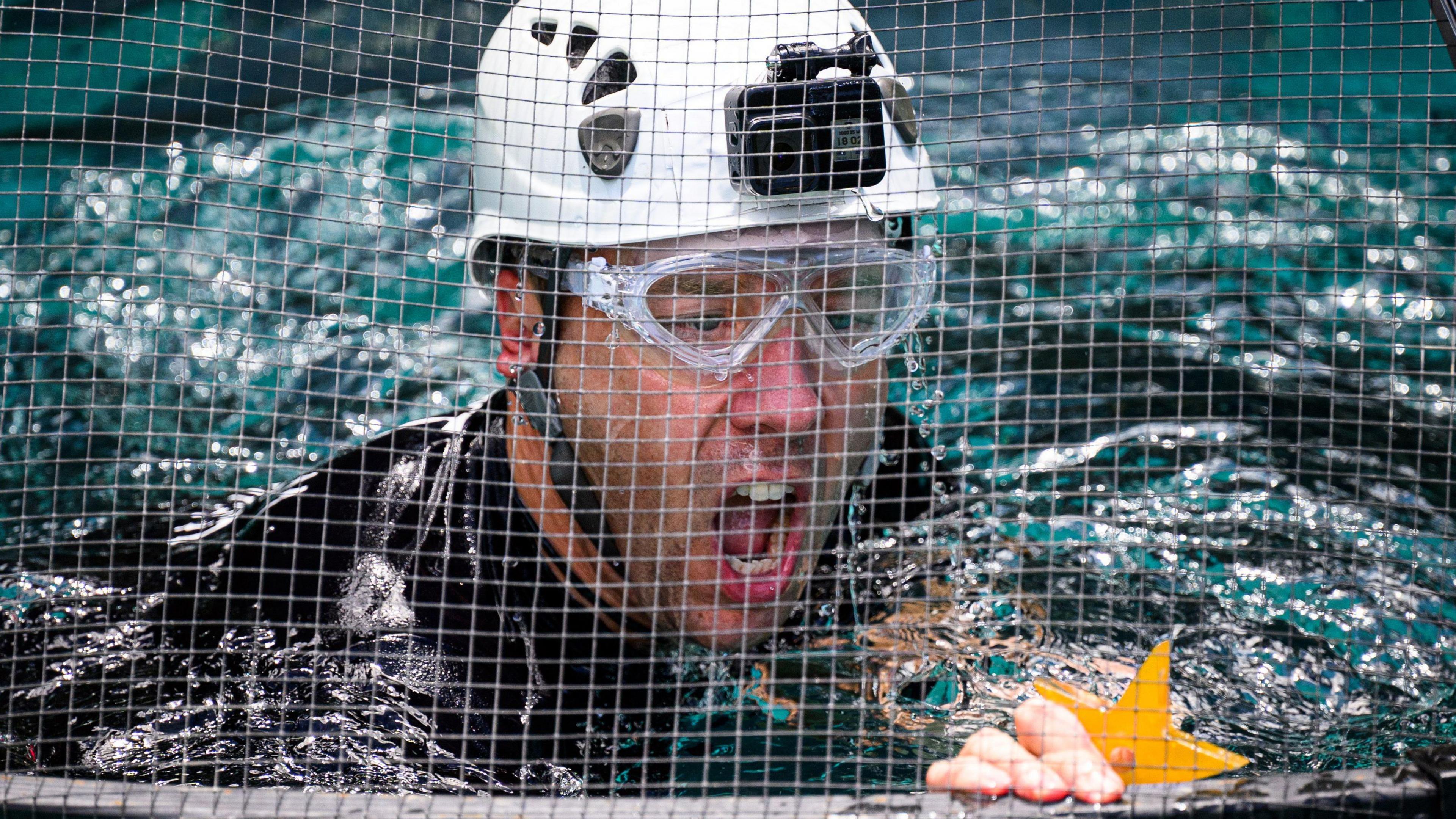Matt Hancock in a water tank with a helpet and goggles and his mouth open, holding a yellow star