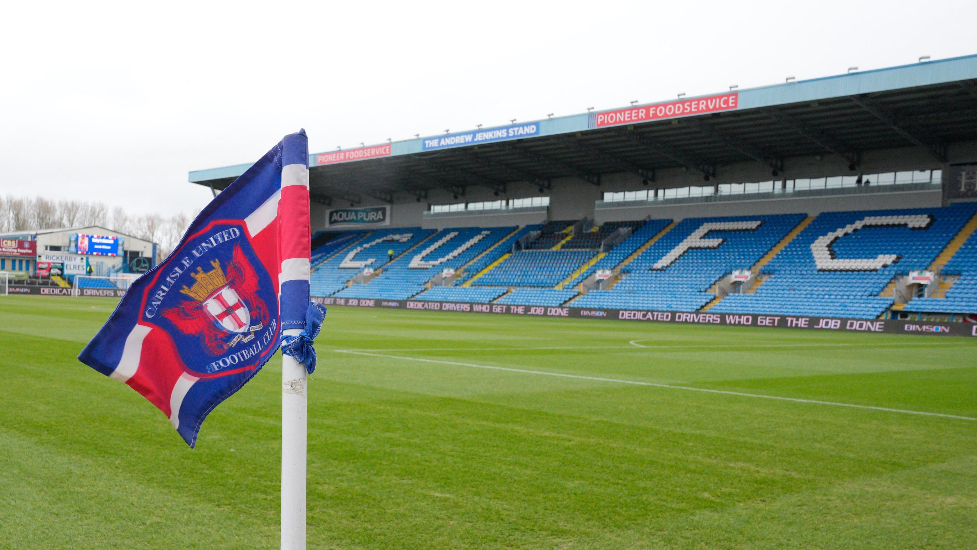 A view of Carlisle's Brunton Park from the corner flag with 'CUFC' on blue seats