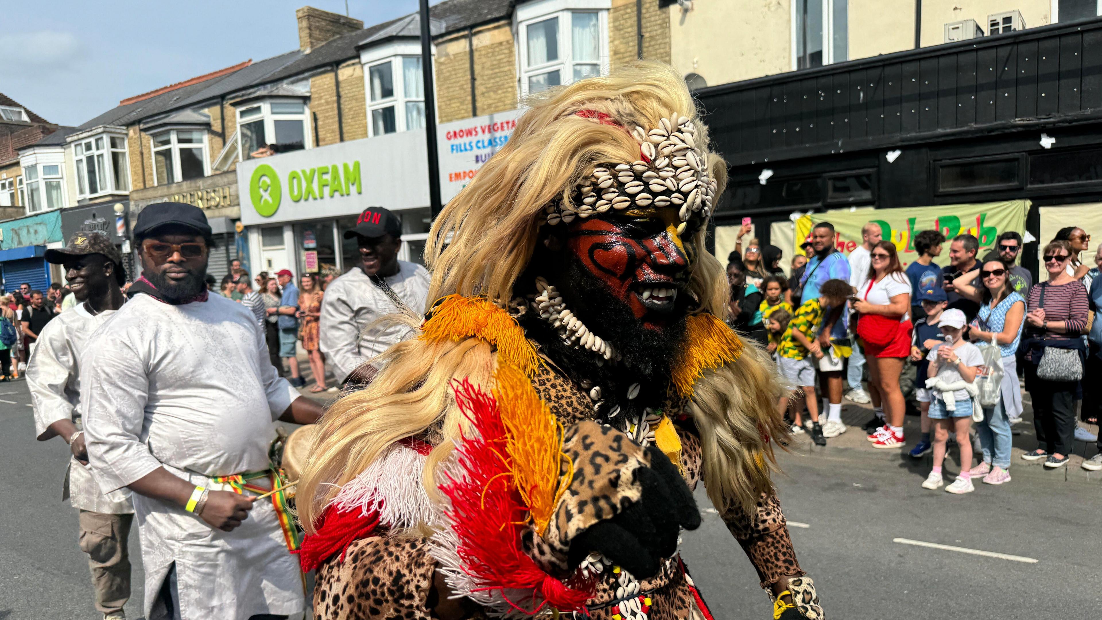 A man wearing leopard print dress with his face painted red black and yellow.