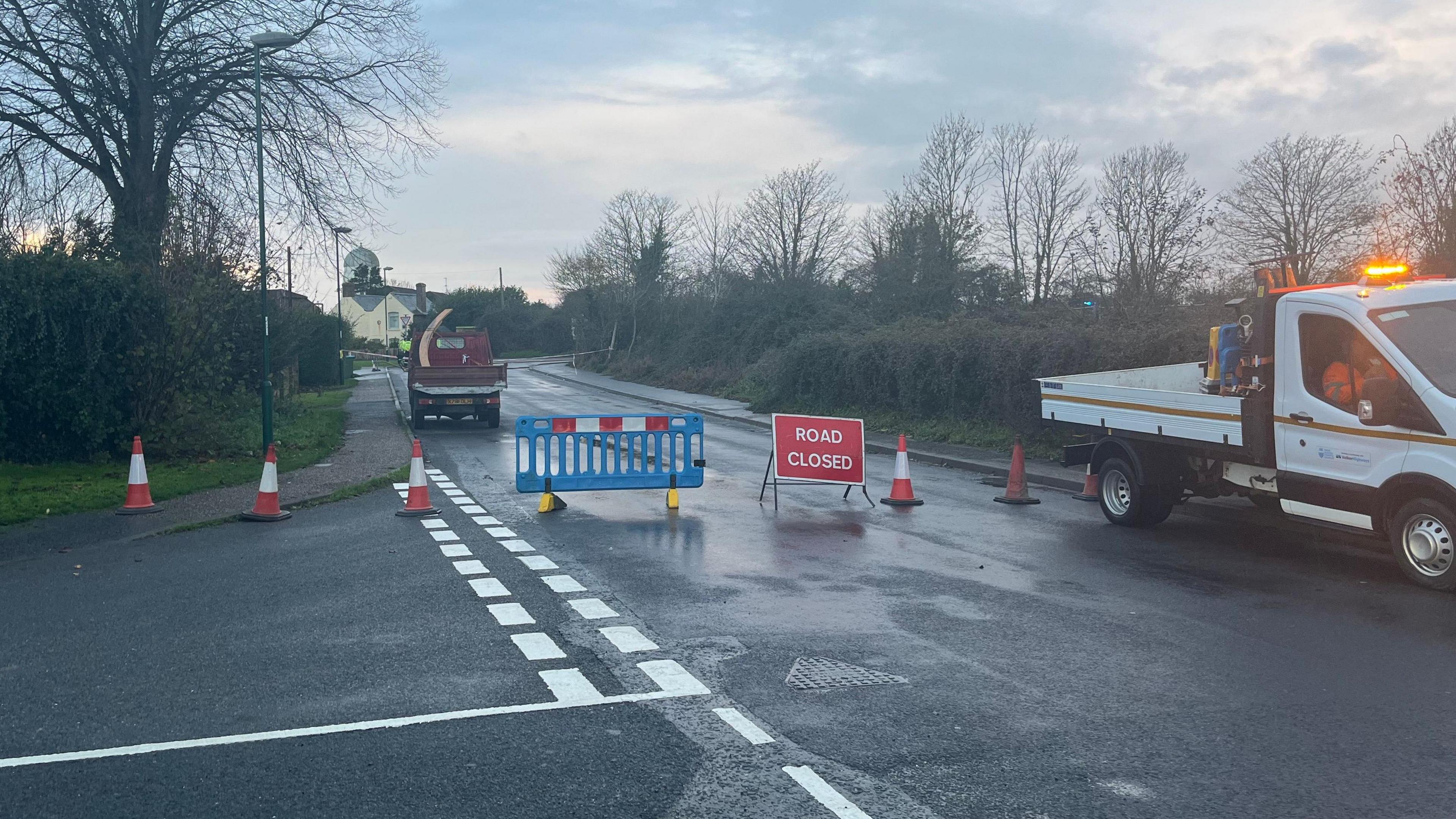 A sign advising that the road is closed on Pagham Road, near Nyetimber, West Sussex, where a car crashed into a gas substation. Several cones are set out on the road.