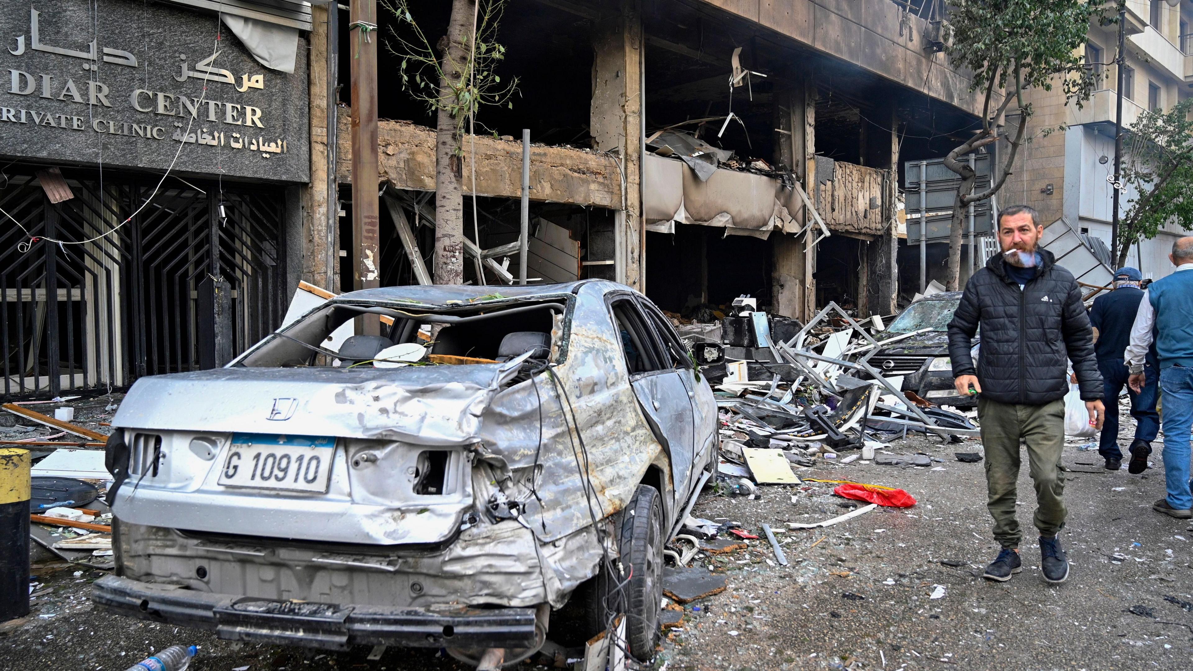 People walk past a building and cars damaged by an Israeli air strike in the Mar Elias area of central Beirut, Lebanon (18 November 2024)