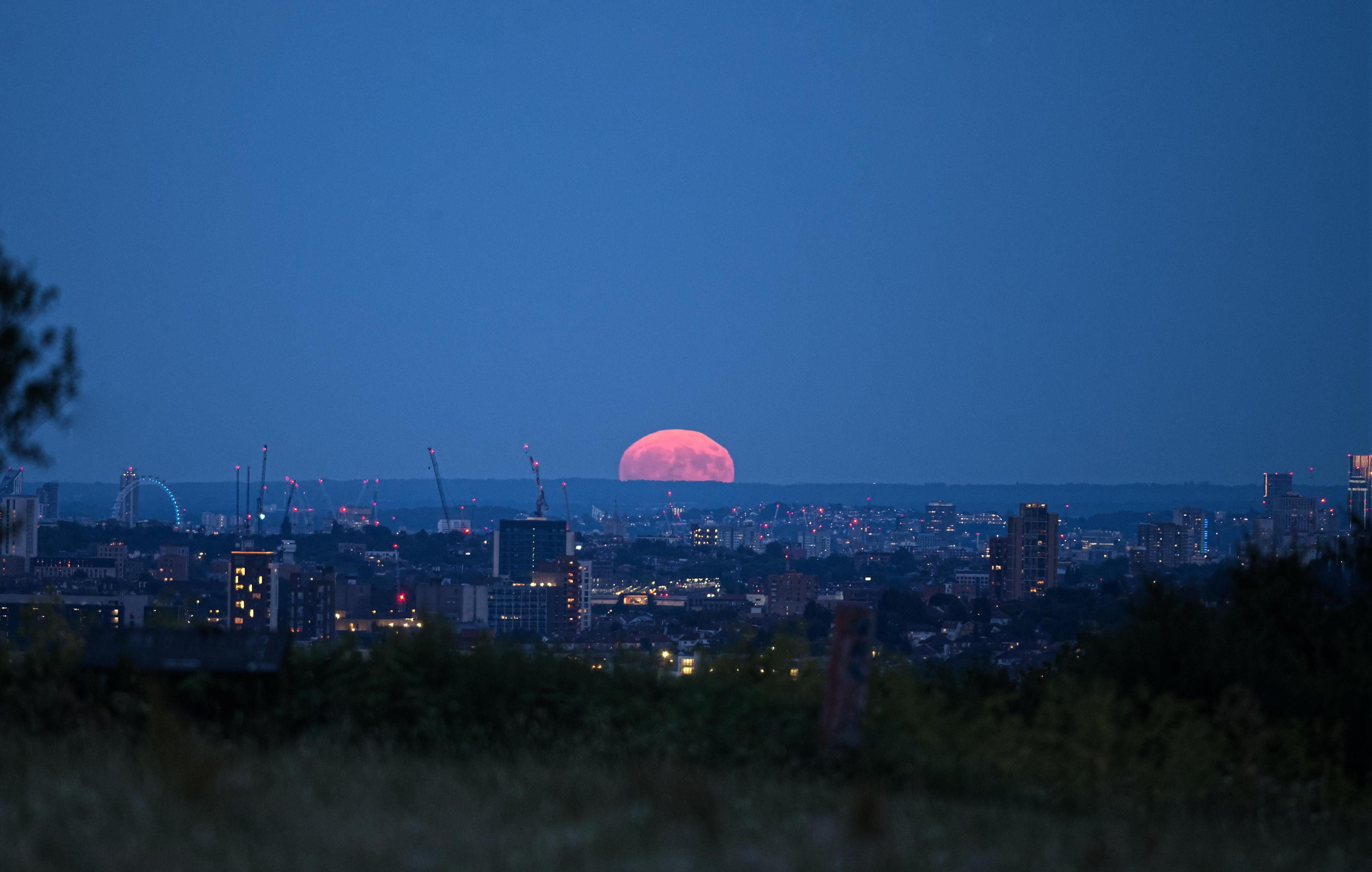 An orange-hued Strawberry Moon sits on the horizon with a city in the foreground