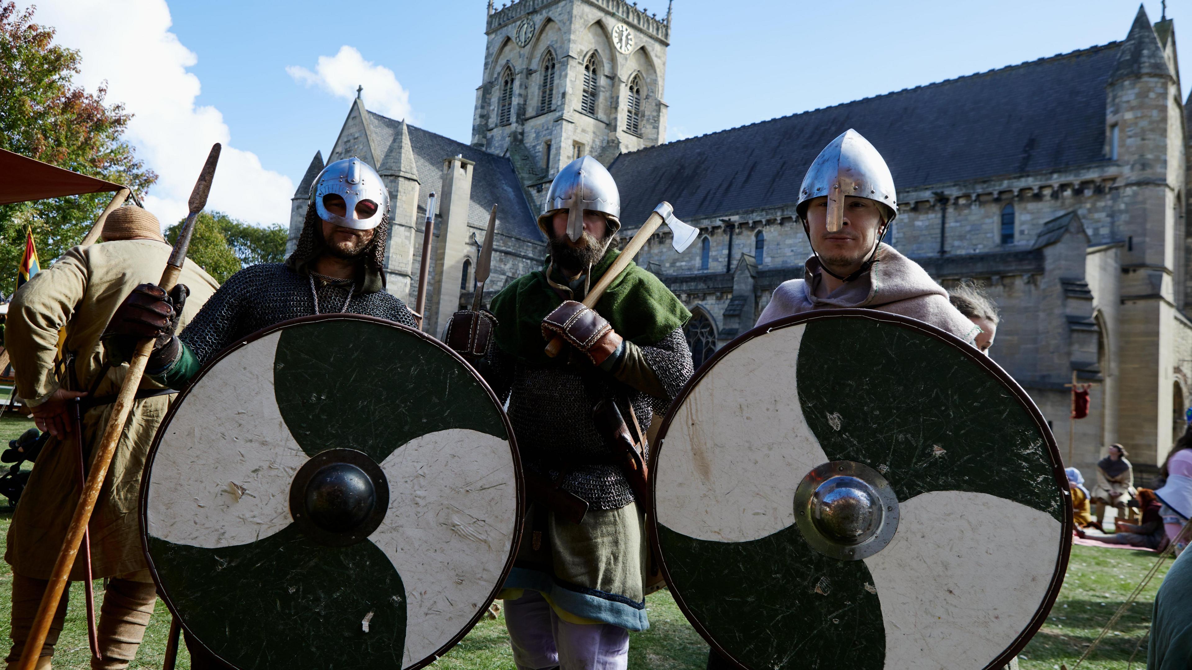 Three men dressed as Vikings, with steel helmets, black-and-white round shields, axes and spears, in front of St James' Church in Grimsby.