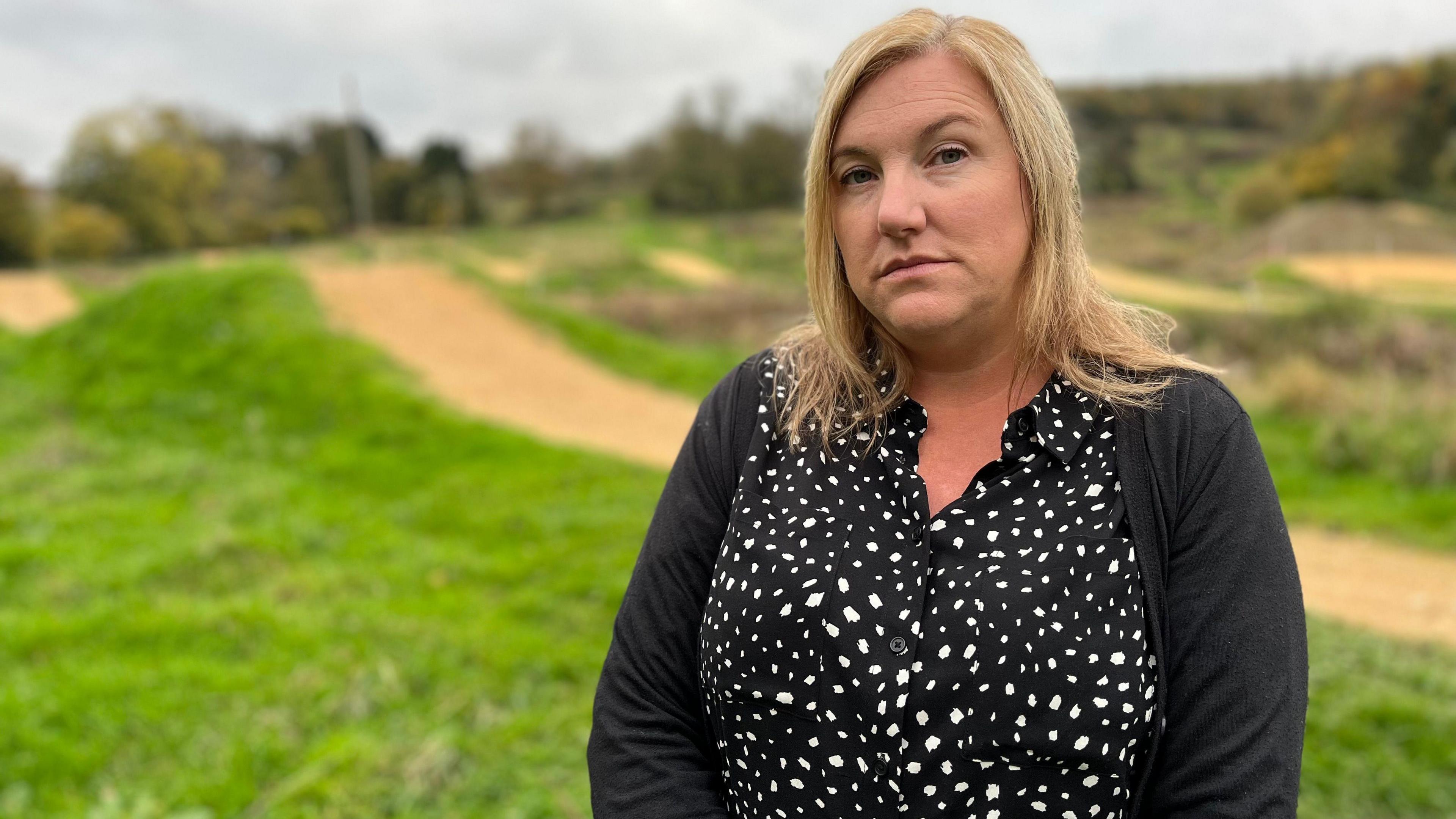 Angela Ruskin photographed at the FlyUp 417 site in Gloucestershire. Angela has long blonde hair and is wearing a black and white spotted blouse with a black cardigan. 