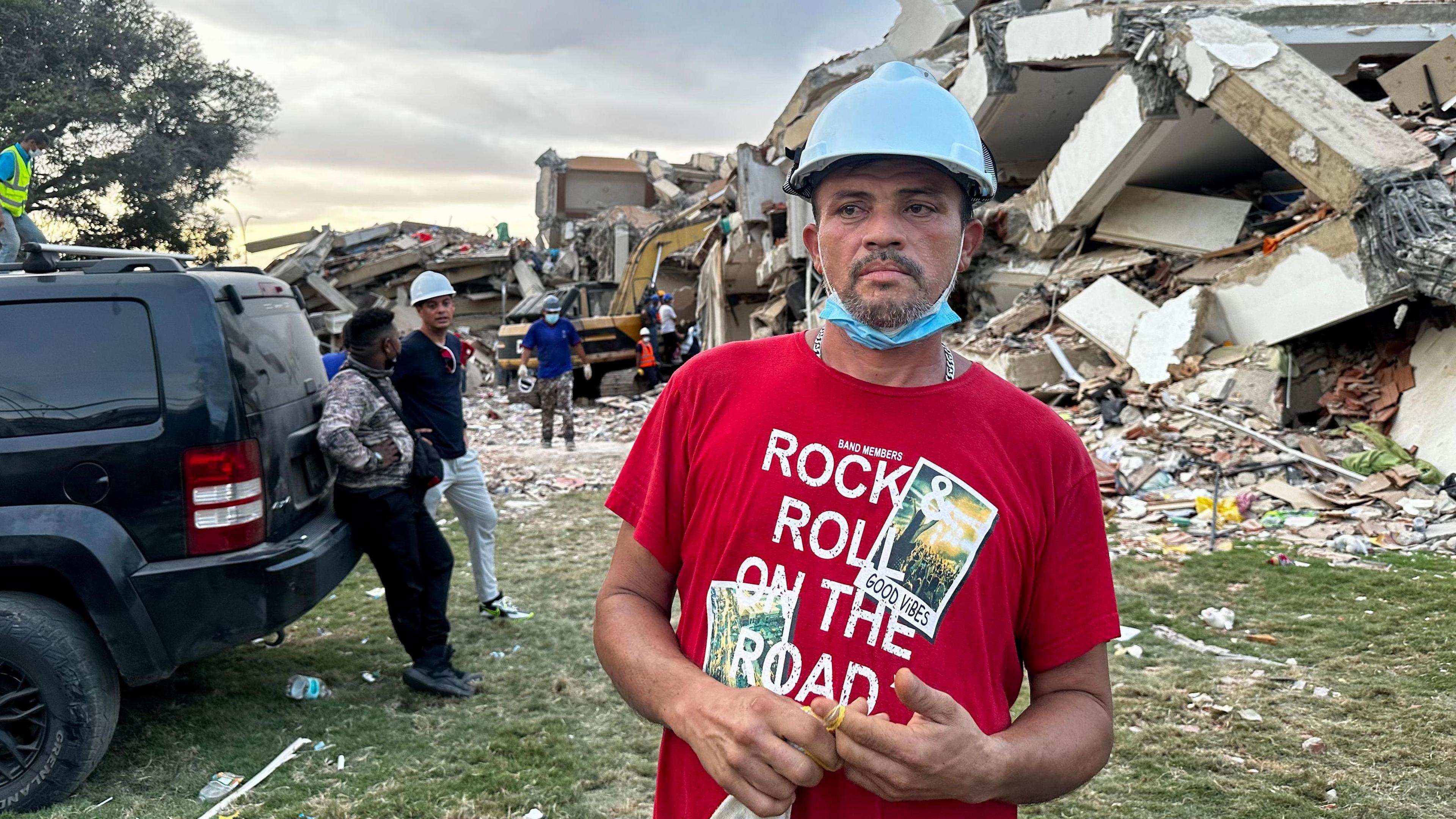 Ronnie Navarro wearing a red flannel top and a blue helmet with the pile of rubble in the background.