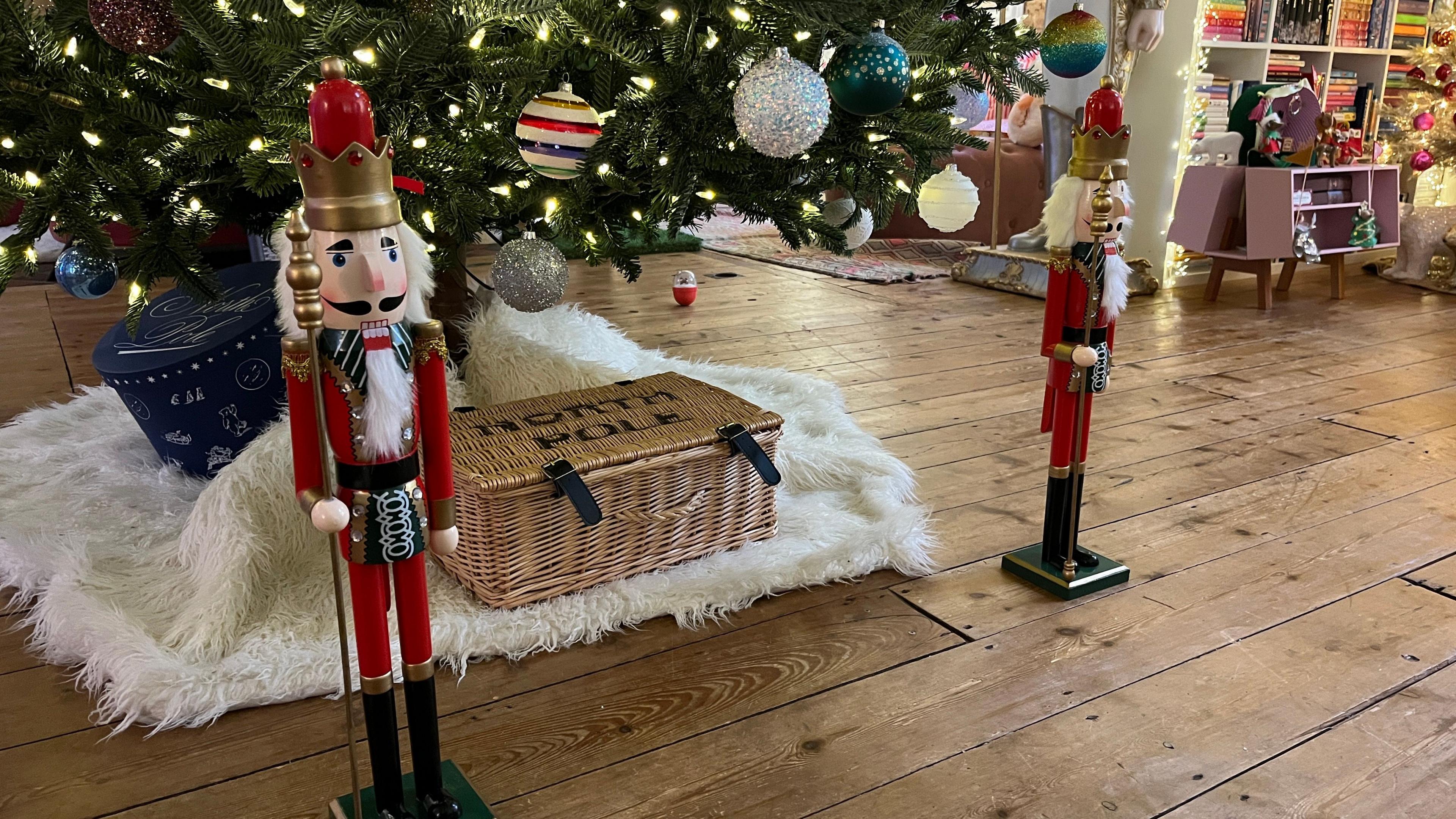 Small nutcracker dolls are sitting under a Christmas tree inside a house
