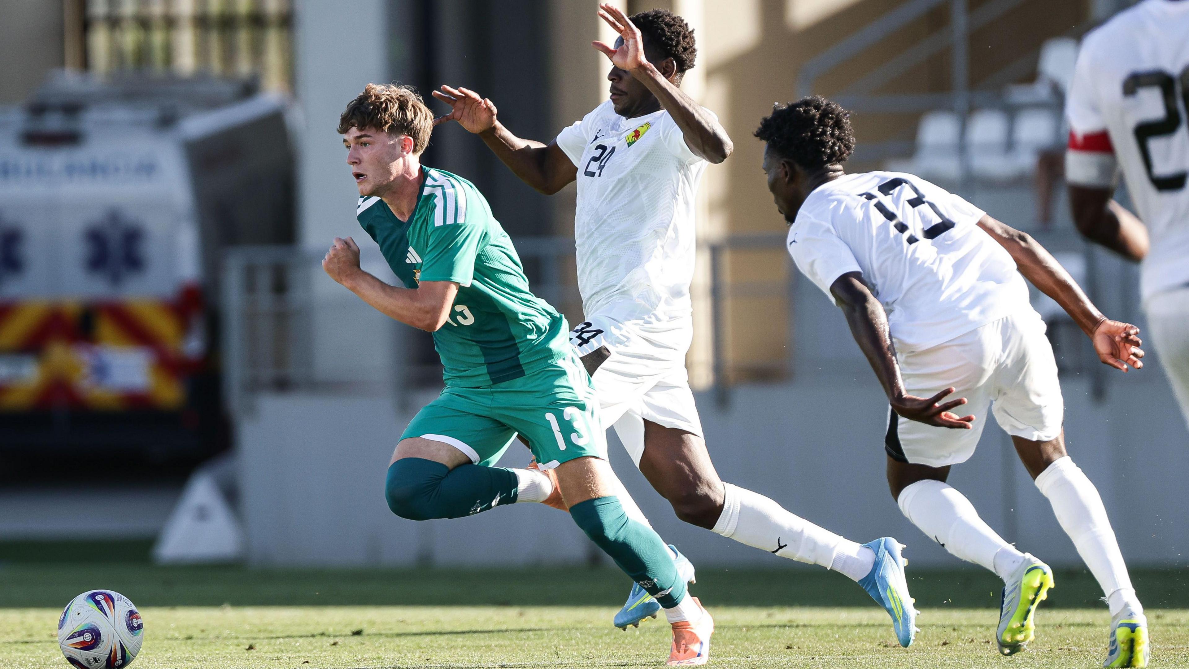 Ceadach O'Neill, in green, moves with the ball, as two Guinea players, in all-white kit, lurk in close attendance