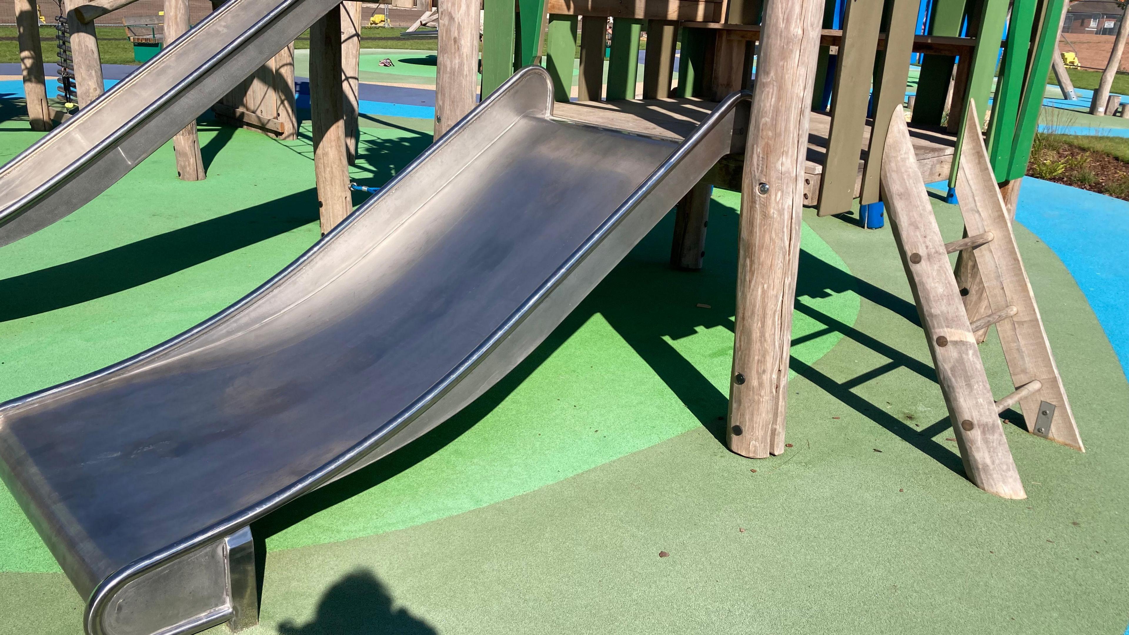 A slide in a children's playground with step ladder-type steps. Another slide can be seen in the background.