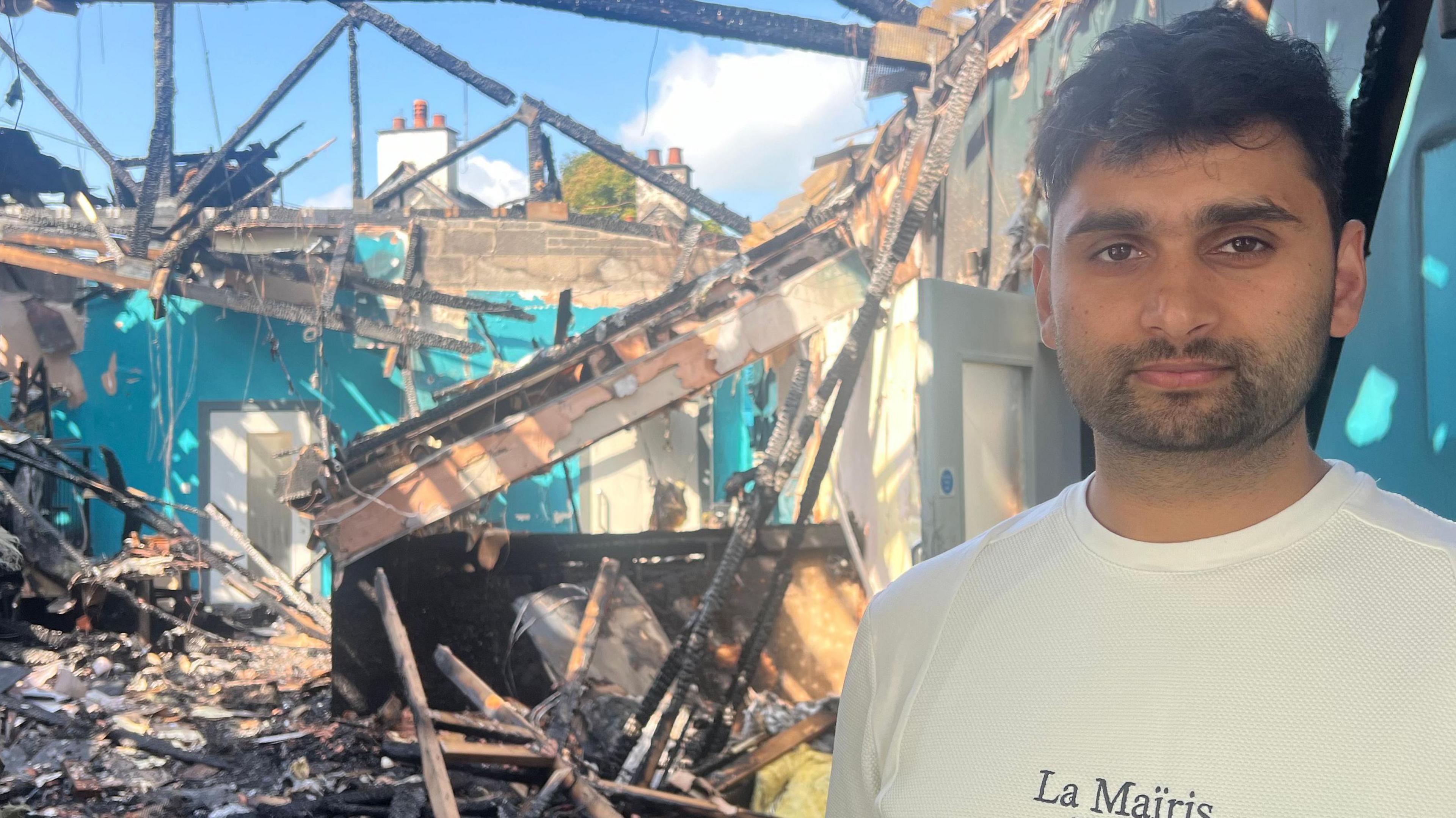 Abjan Acharya in a white tshirt stood outside a badly fire-damaged bar in Newtownabbey