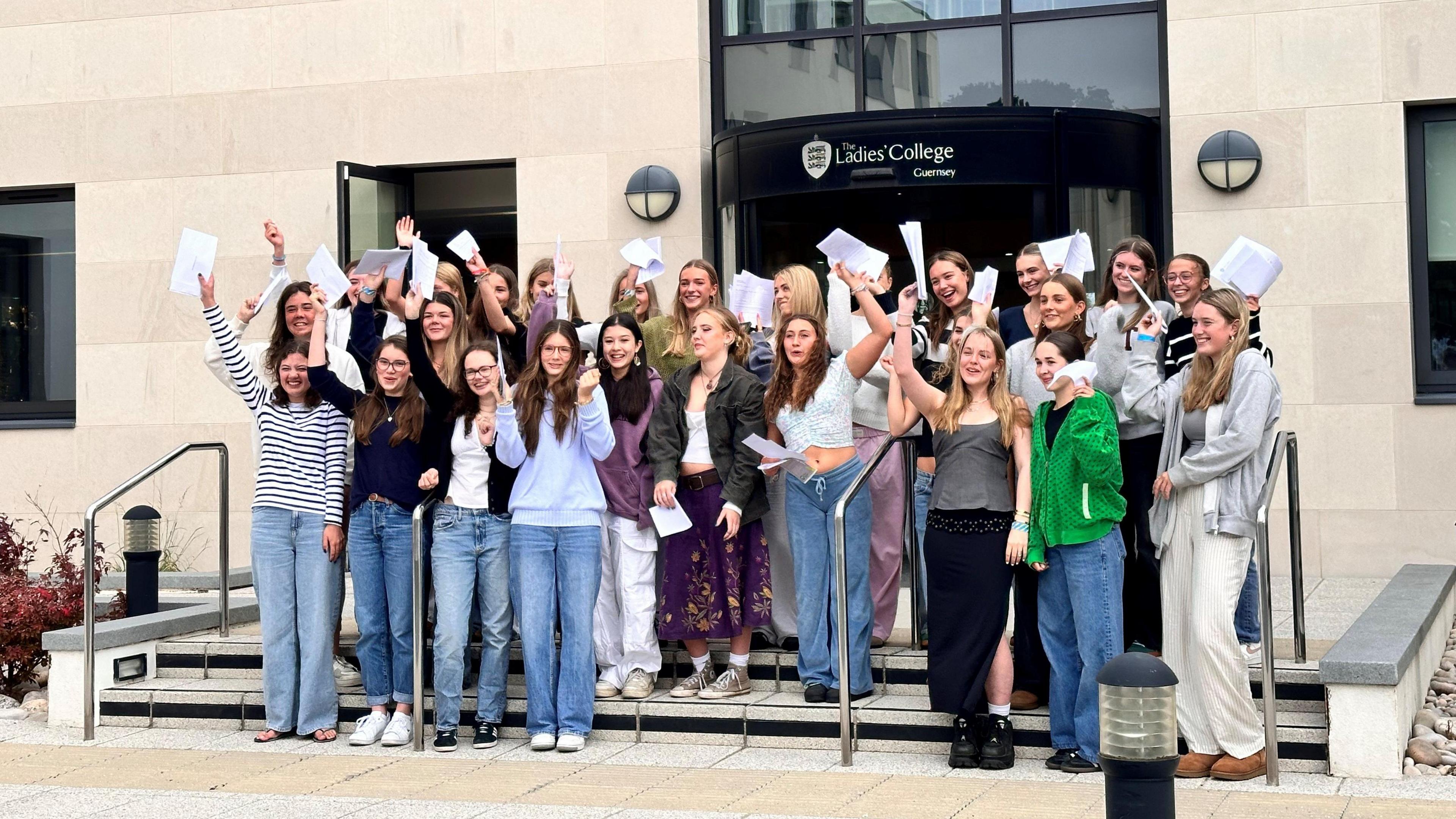 Students on the steps of Ladies' College holding their exam results in the air