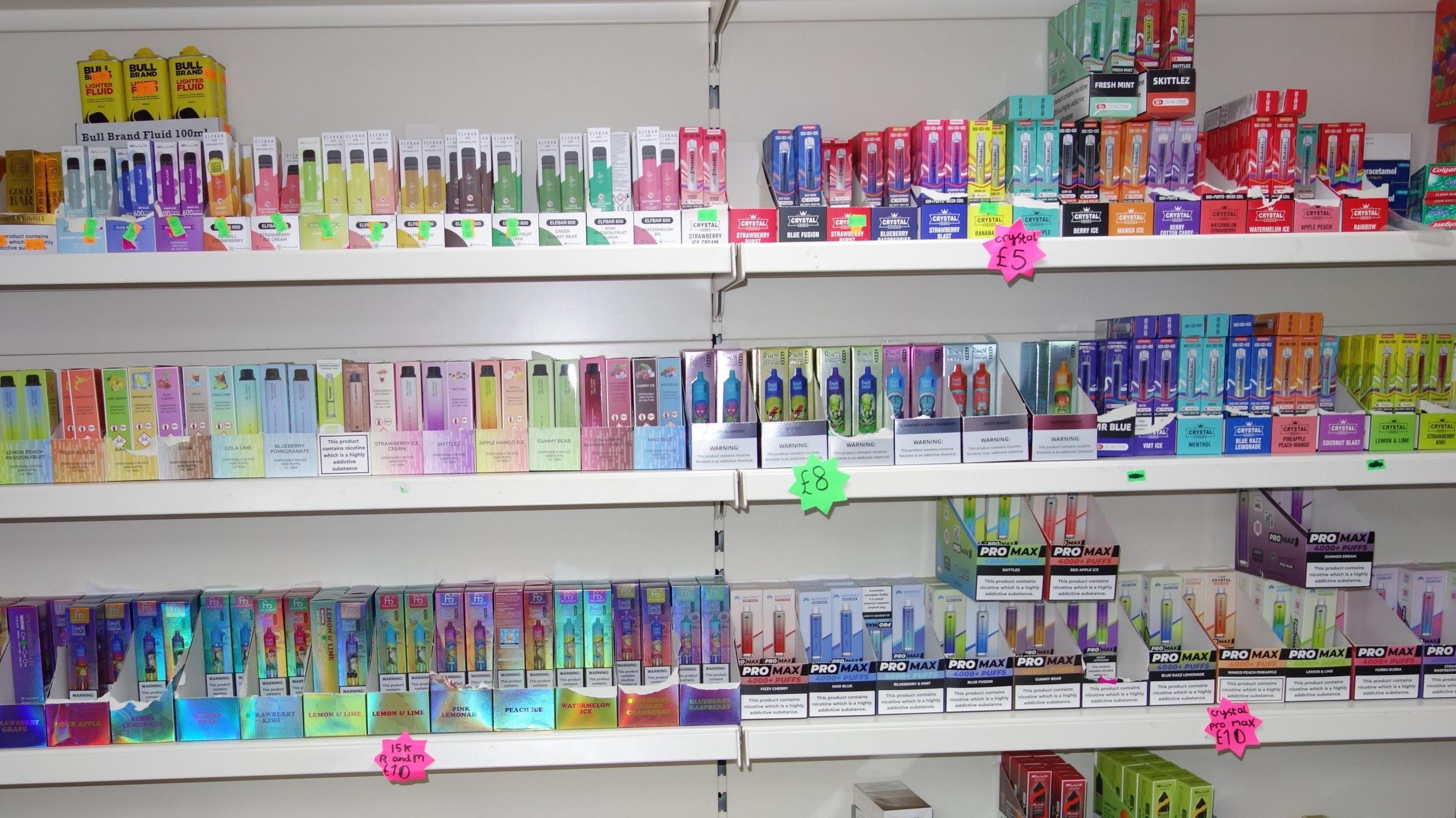 Rows of brightly-coloured vapes  in packaging on white shelves