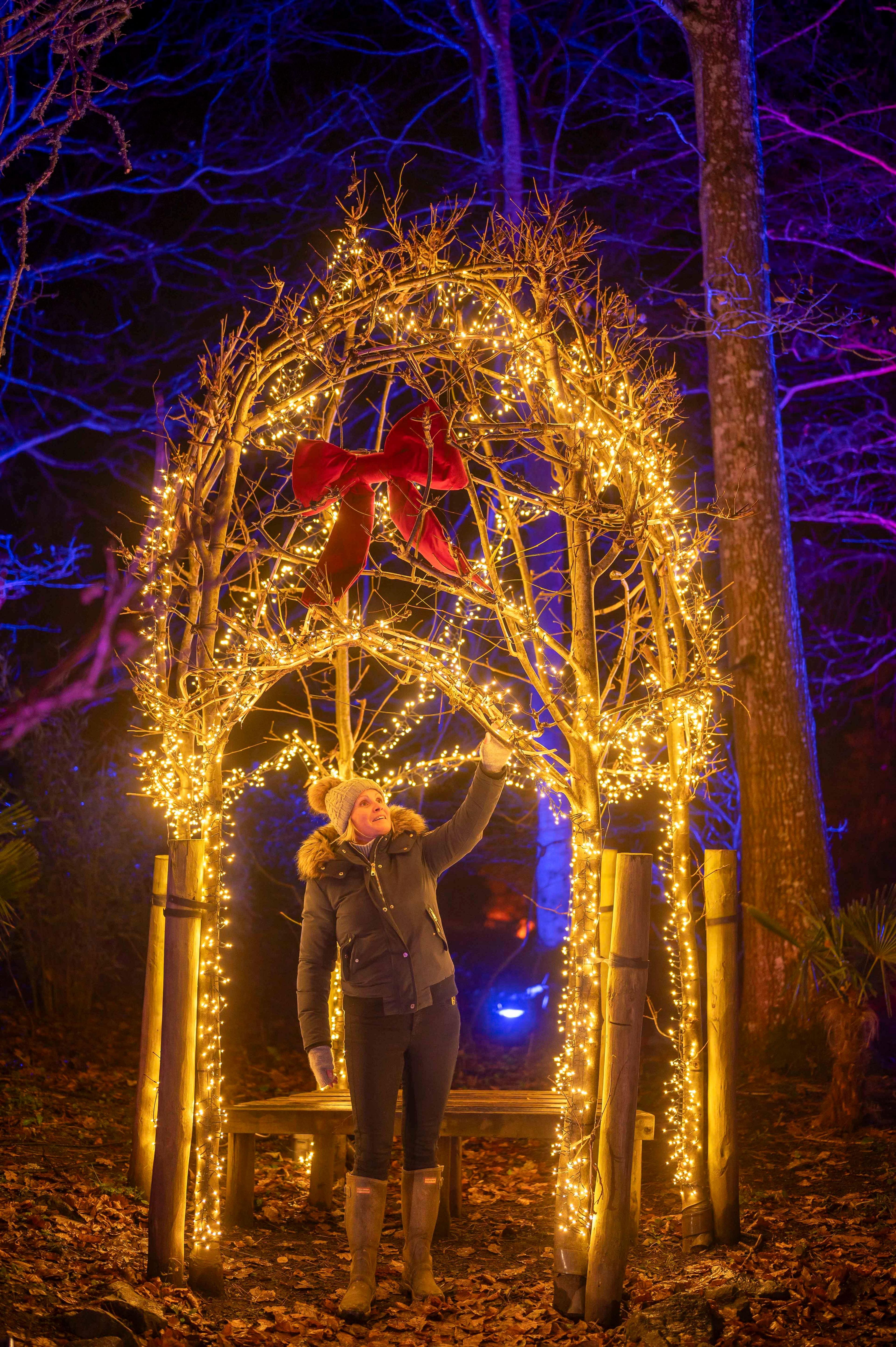 A woman stands under an archway of lights with a bow on the front of it