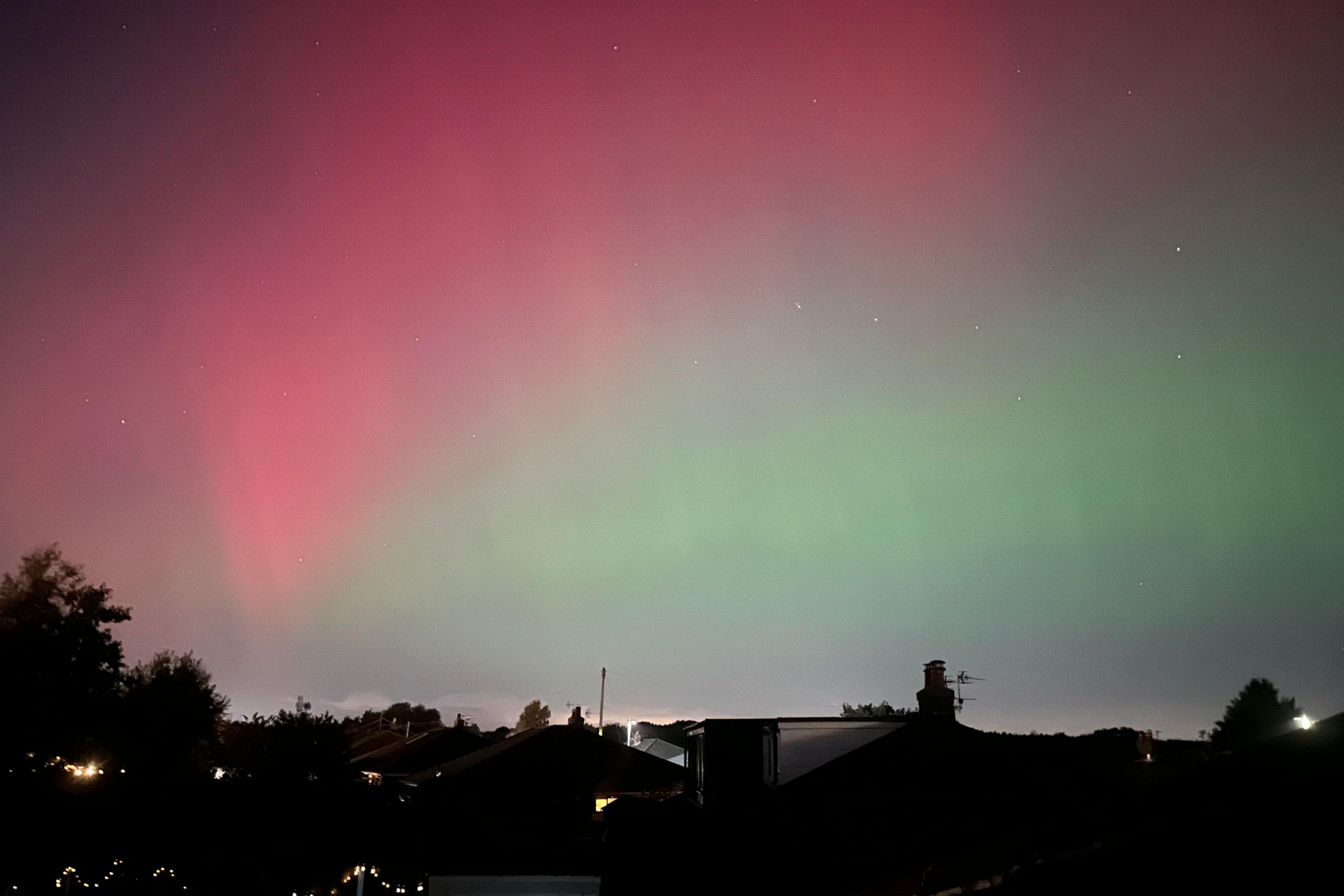 Stars shine among shades of pink and green above houses and tree