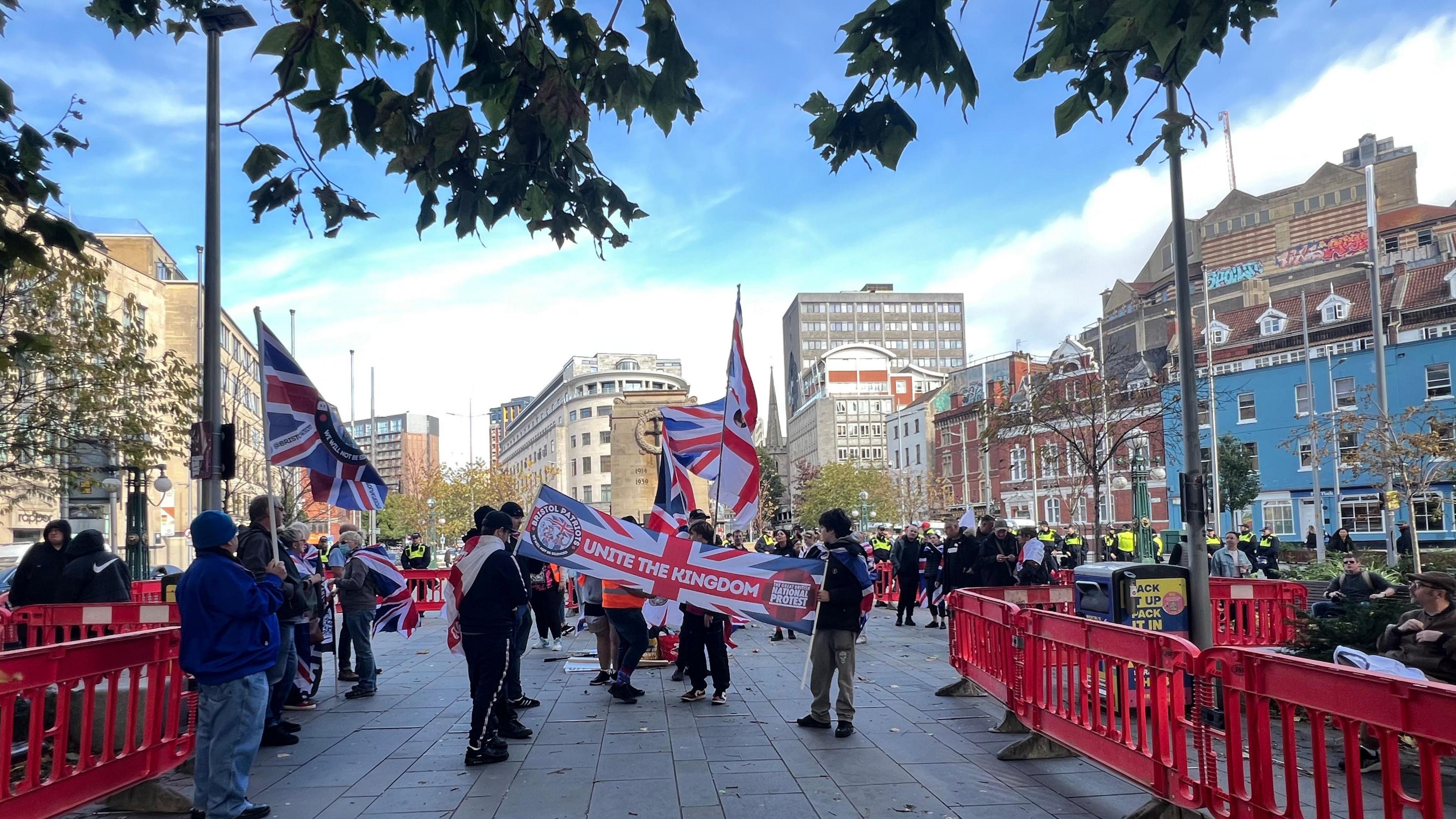 A Unite the Kingdom banner held by two people, with more protesters behind holding flags. They are surrounded by red barriers