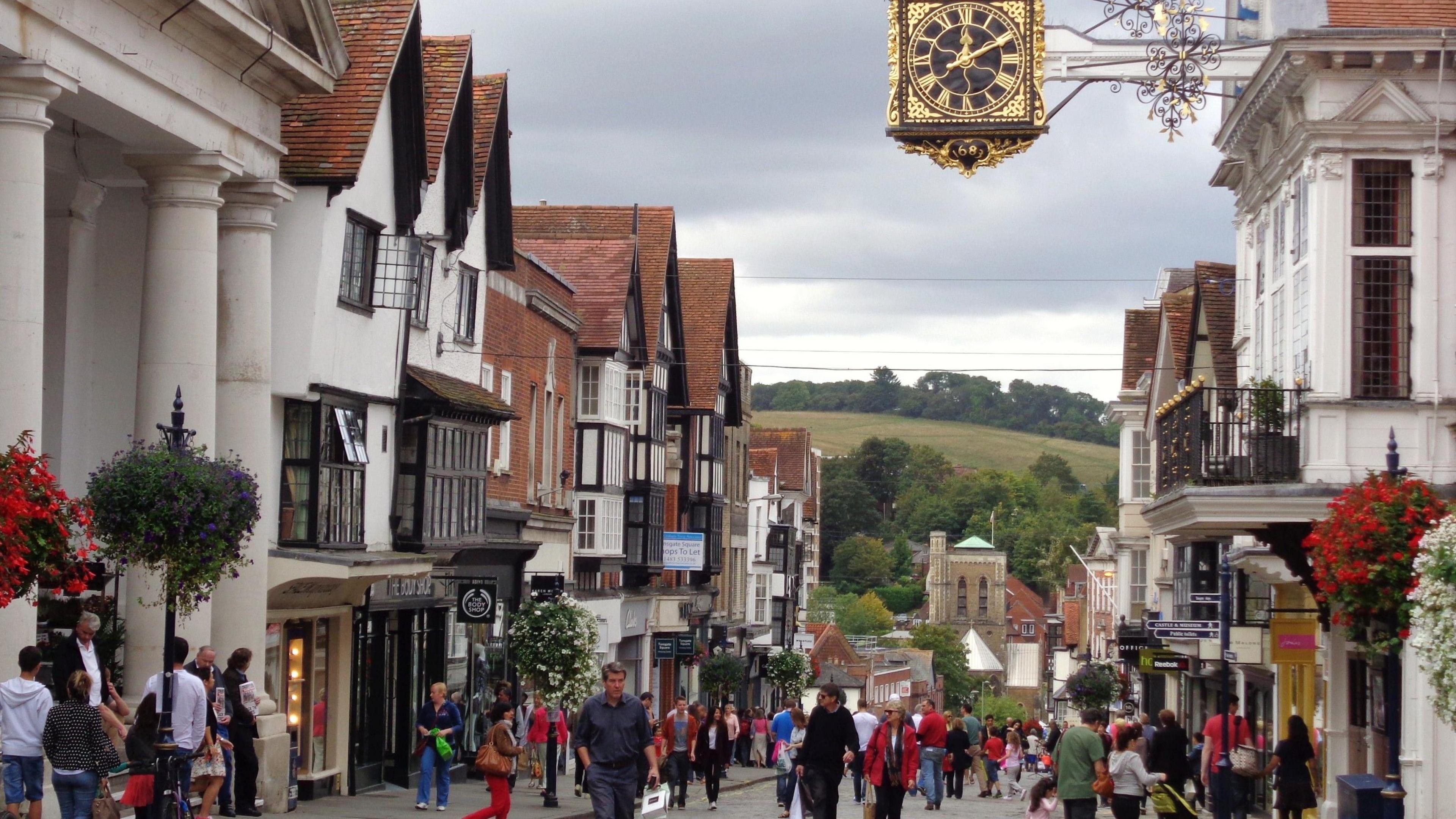 The centre of Guildford, with people walking down the High Street and a civic clock showing ten minutes past twelve.