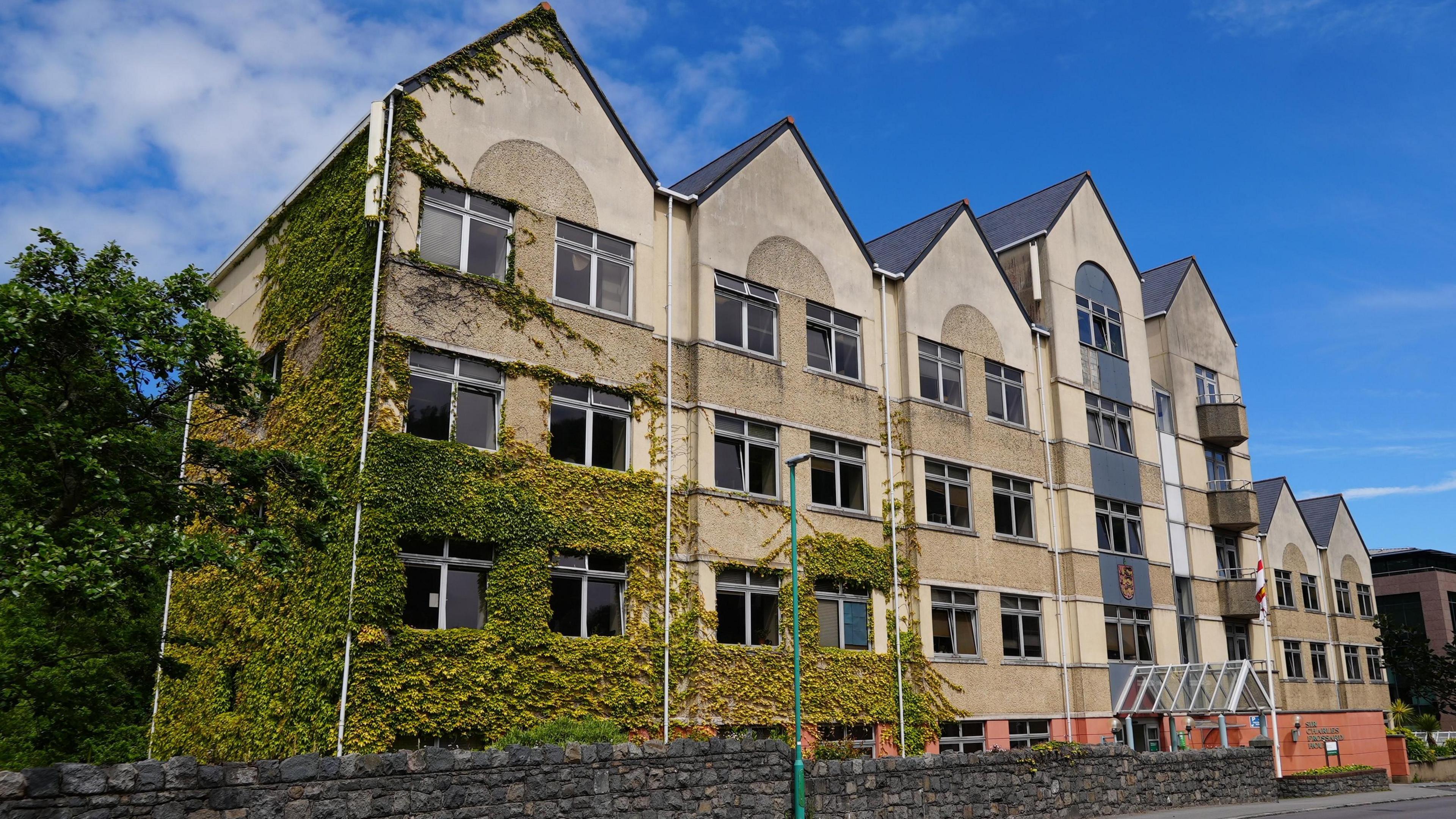 A large yellow building with seven triangular points and creeping green ivy on the left hand side of the building. 