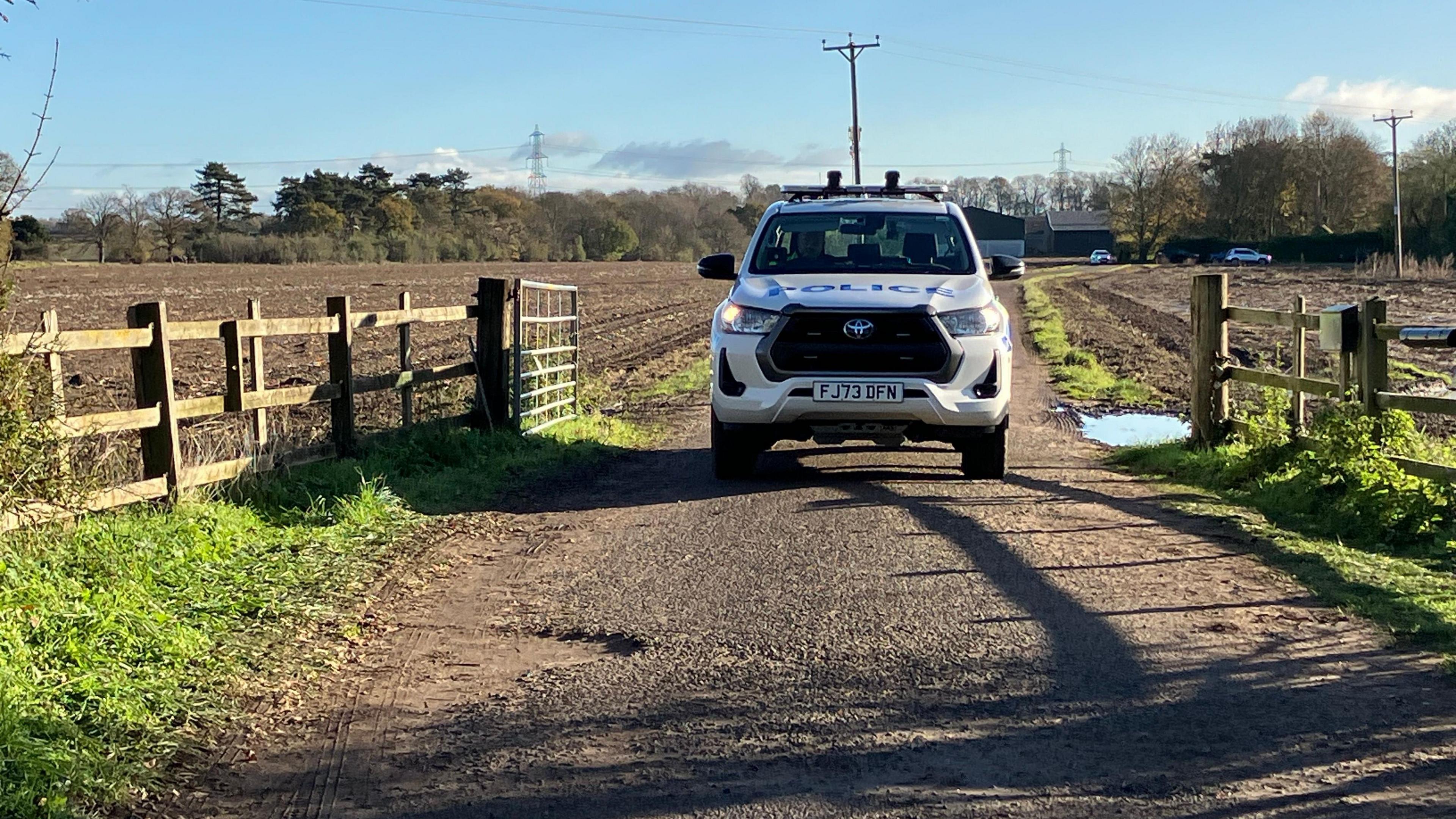 A police truck is parked along a pathway leading towards a farm
