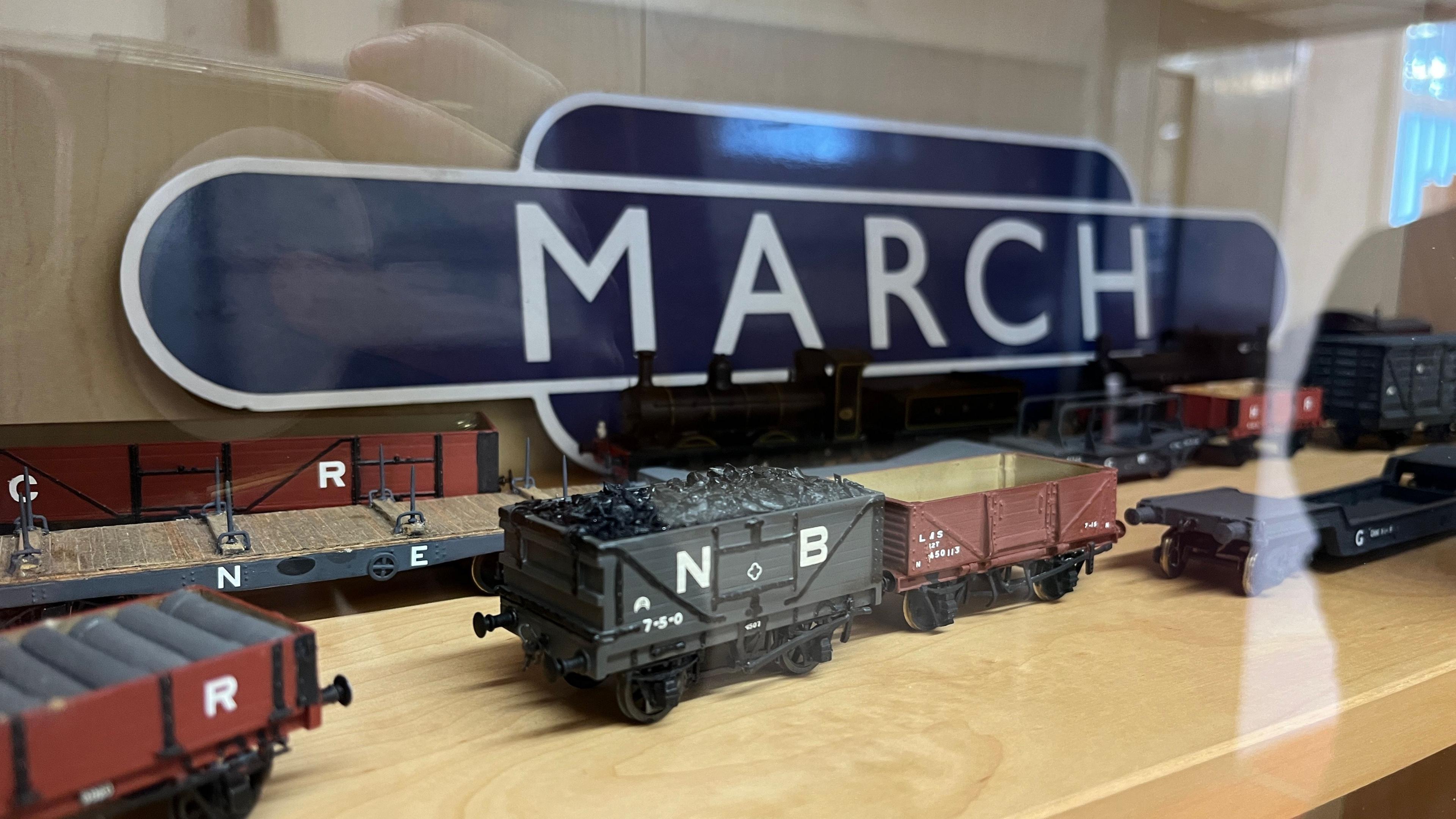 A model of part of the old station has a large blue sign with the word "March" printed in white. There are train carriages carrying various things including coal in front of the sign