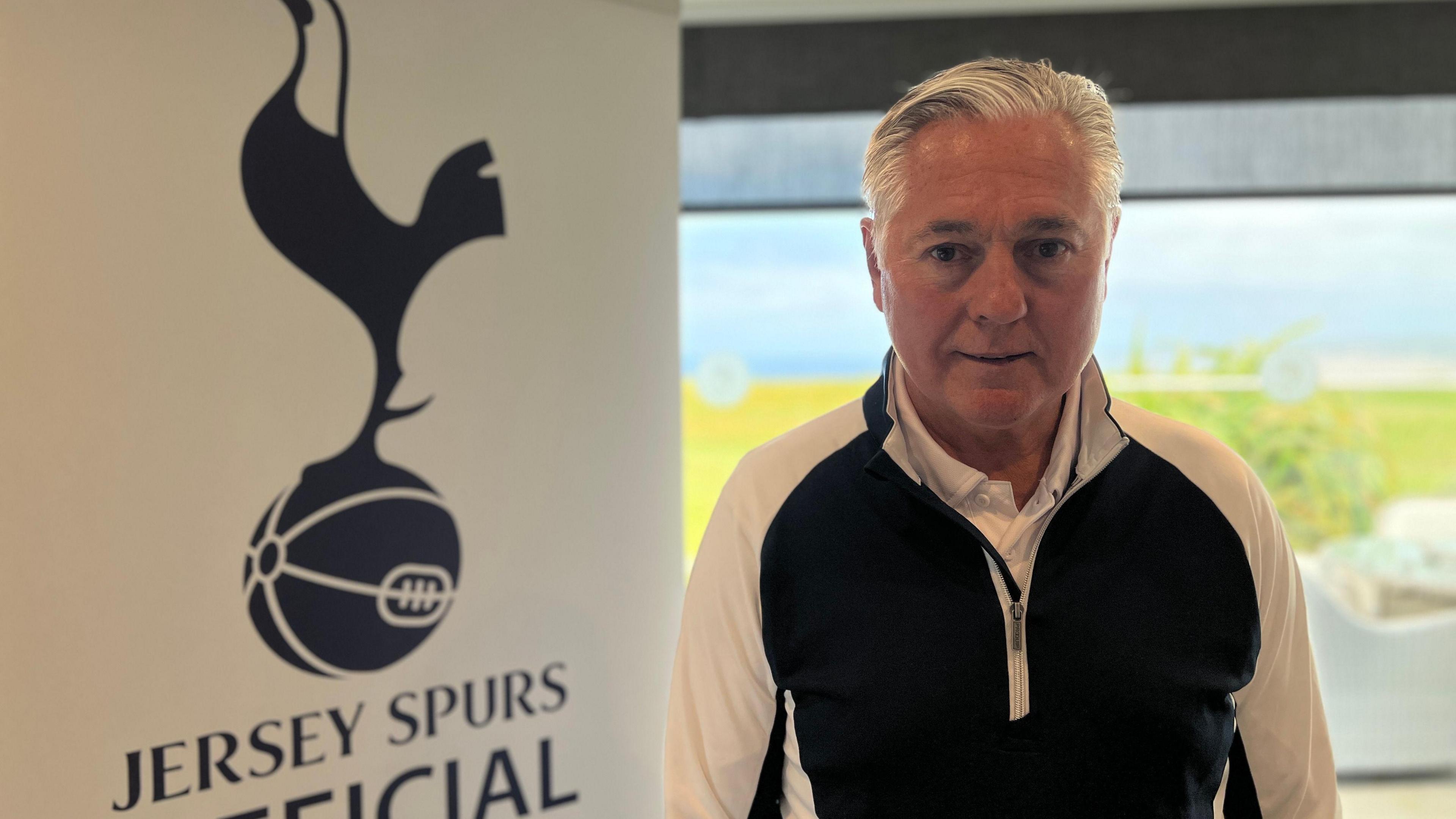 Paul looks at the camera as he stands next to a Jersey Spurs Supporters banner