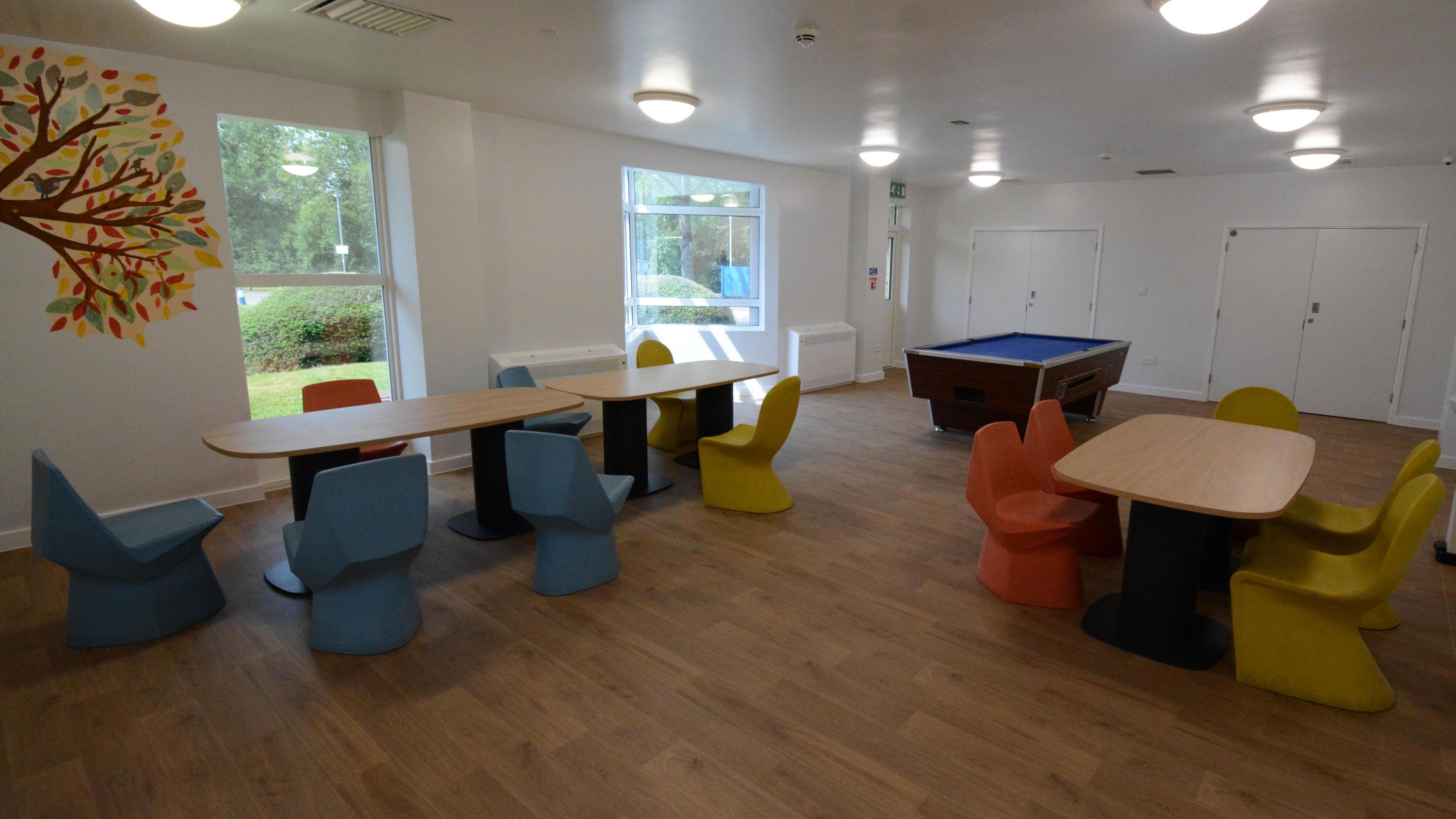 A room with a wooden floor, white walls and tables with colourful tables around them.