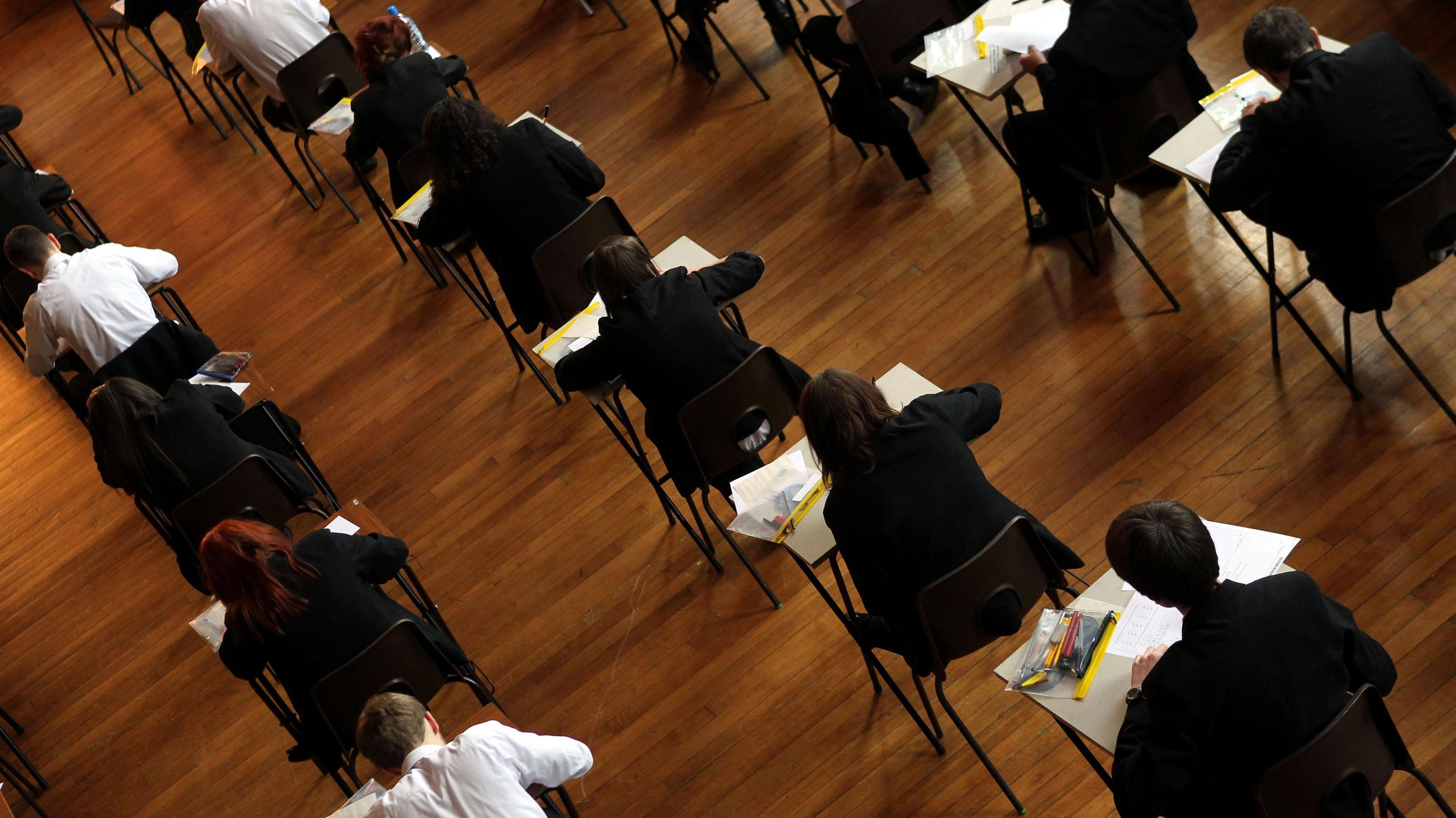 Students in an exam hall taking an exam. They are in rows and wearing shirts and black blazers.